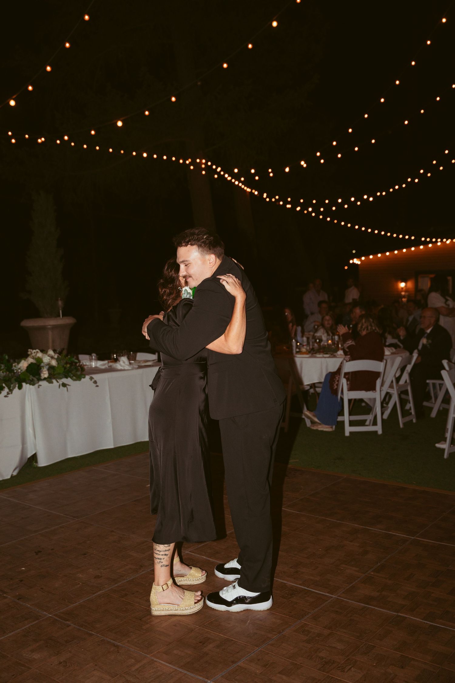 A couple shares a slow dance on an outdoor dance floor under twinkling lights.