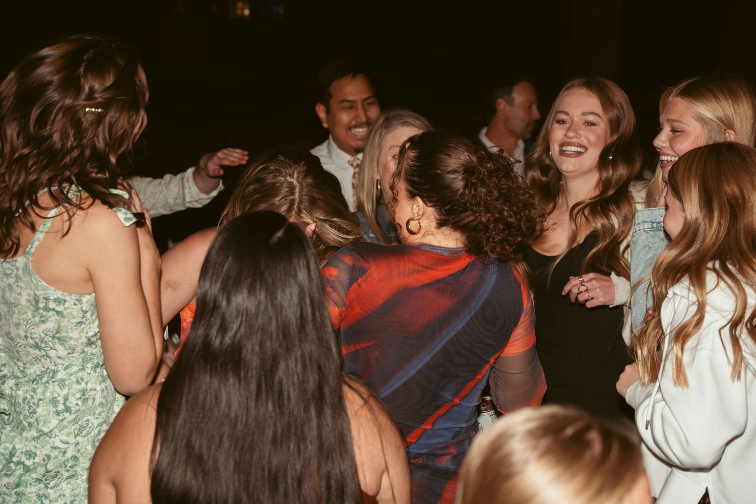 Energetic crowd dancing and celebrating at wedding reception under dim lighting.