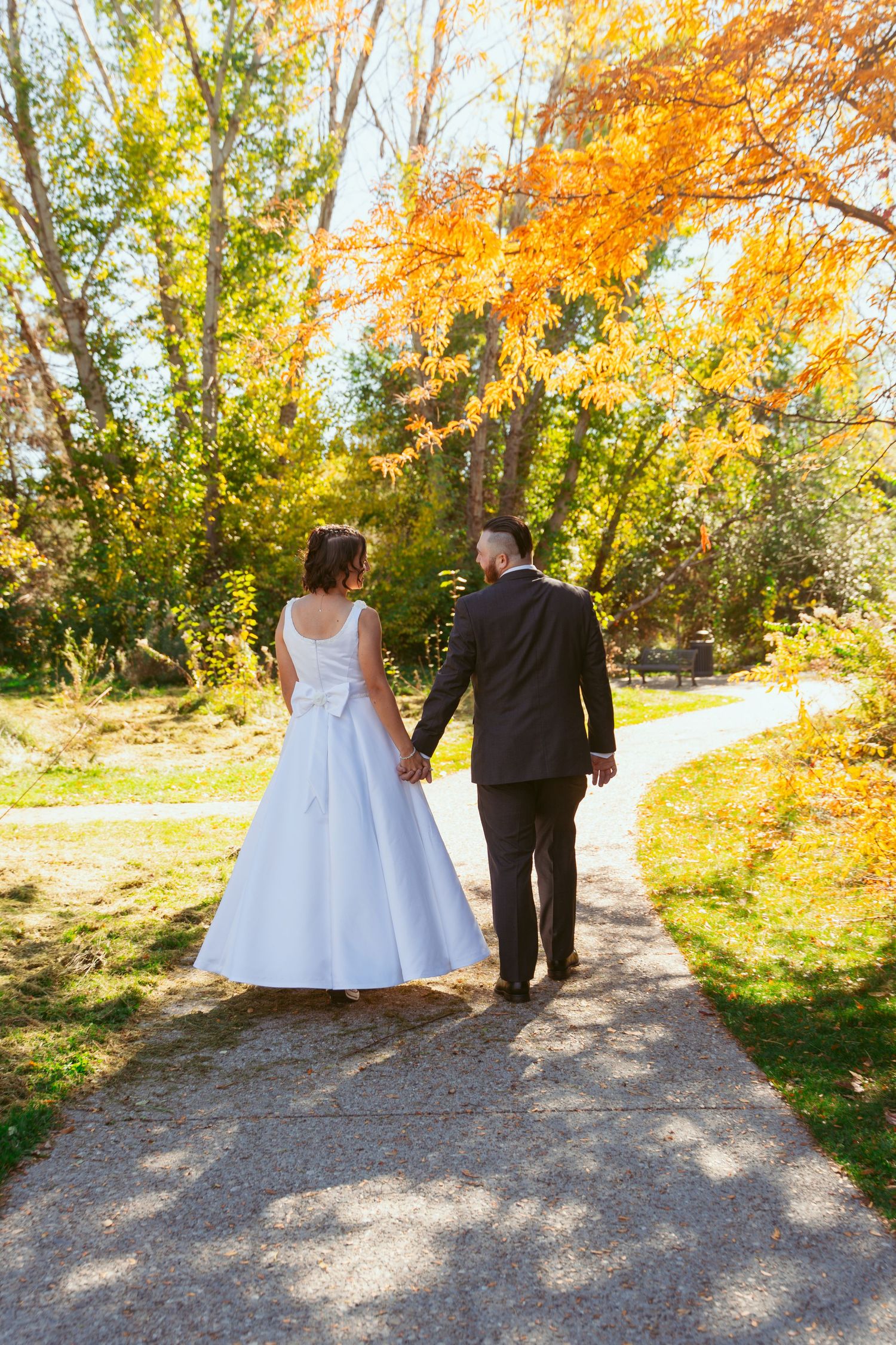 A couple takes a romantic walk on a winding path amid autumn trees and golden light.