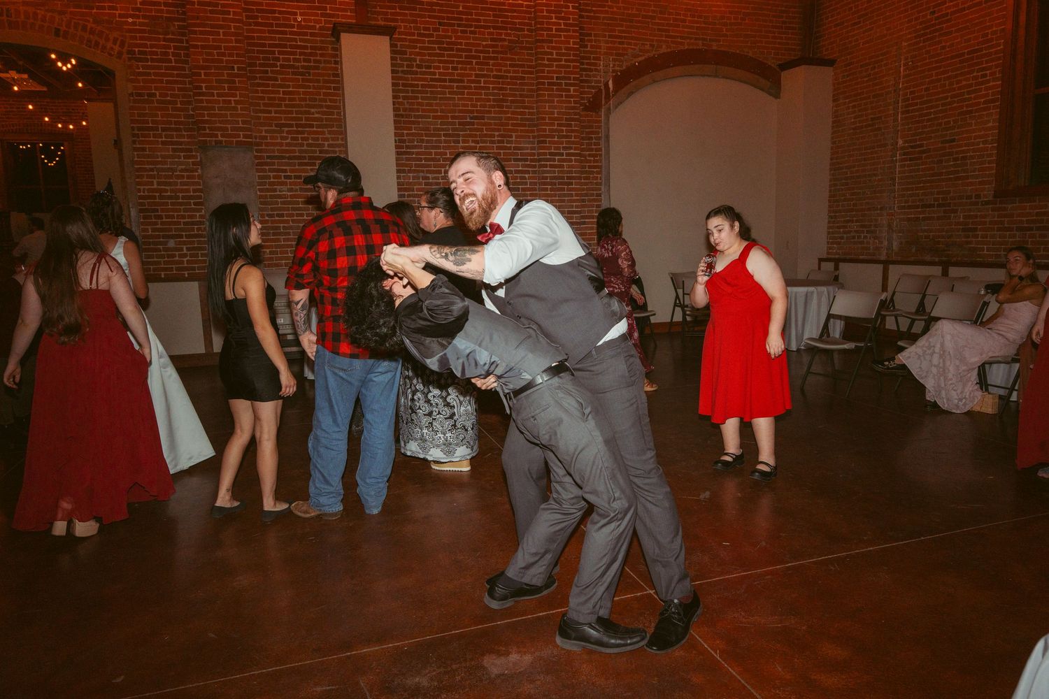Couples performing dramatic dance moves in a rustic venue with exposed brick walls and string lights.