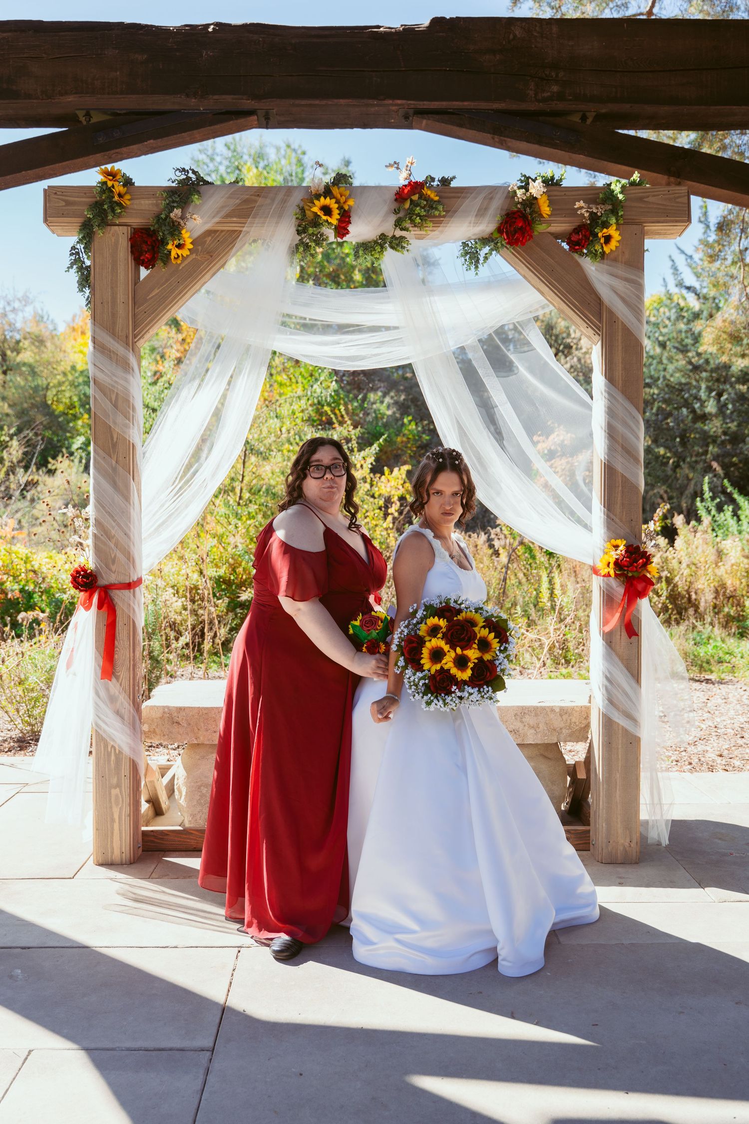 Outdoor wedding ceremony setup with white draping, red accents, and sunflower decorations.