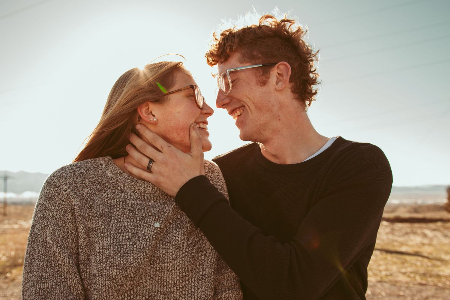 Romantic couple embraces in warm sunlight against desert landscape during golden hour photoshoot.