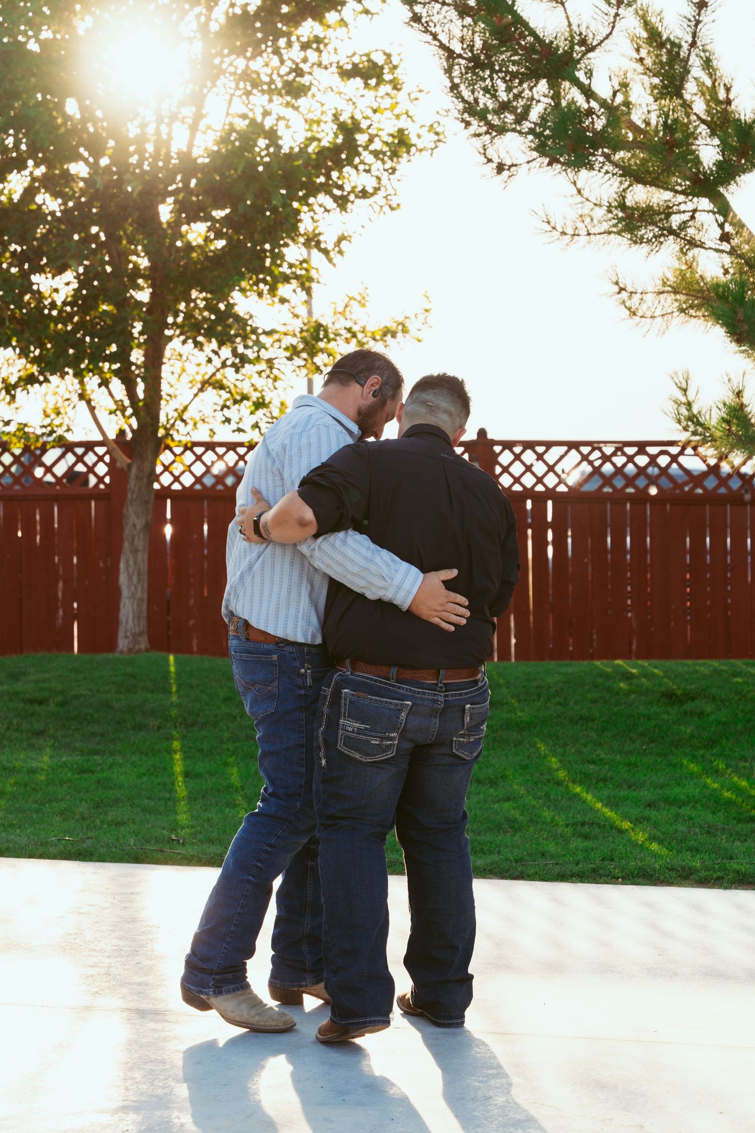 A group of people dancing together in a line on an outdoor patio at sunset with a wooden fence in the background.