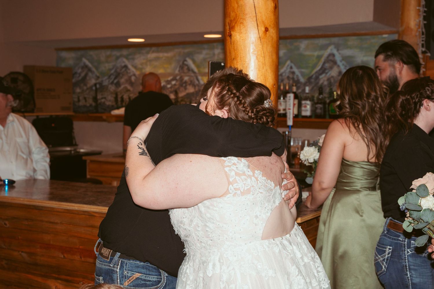 Wedding guests dancing and embracing on a wooden dance floor with rustic wooden pillars in the background.
