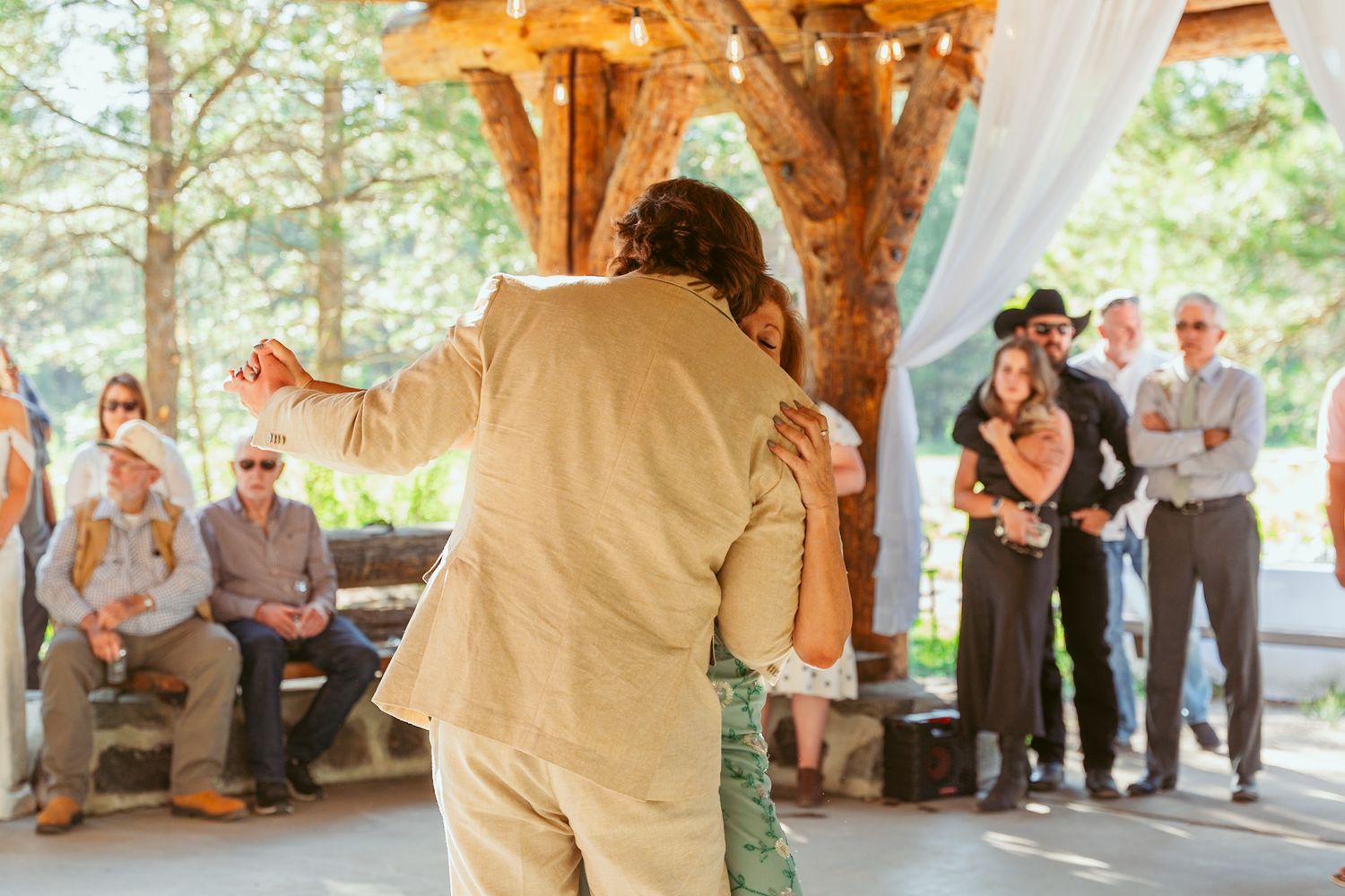 Dancers performing under wooden beams with natural forest backdrop visible.