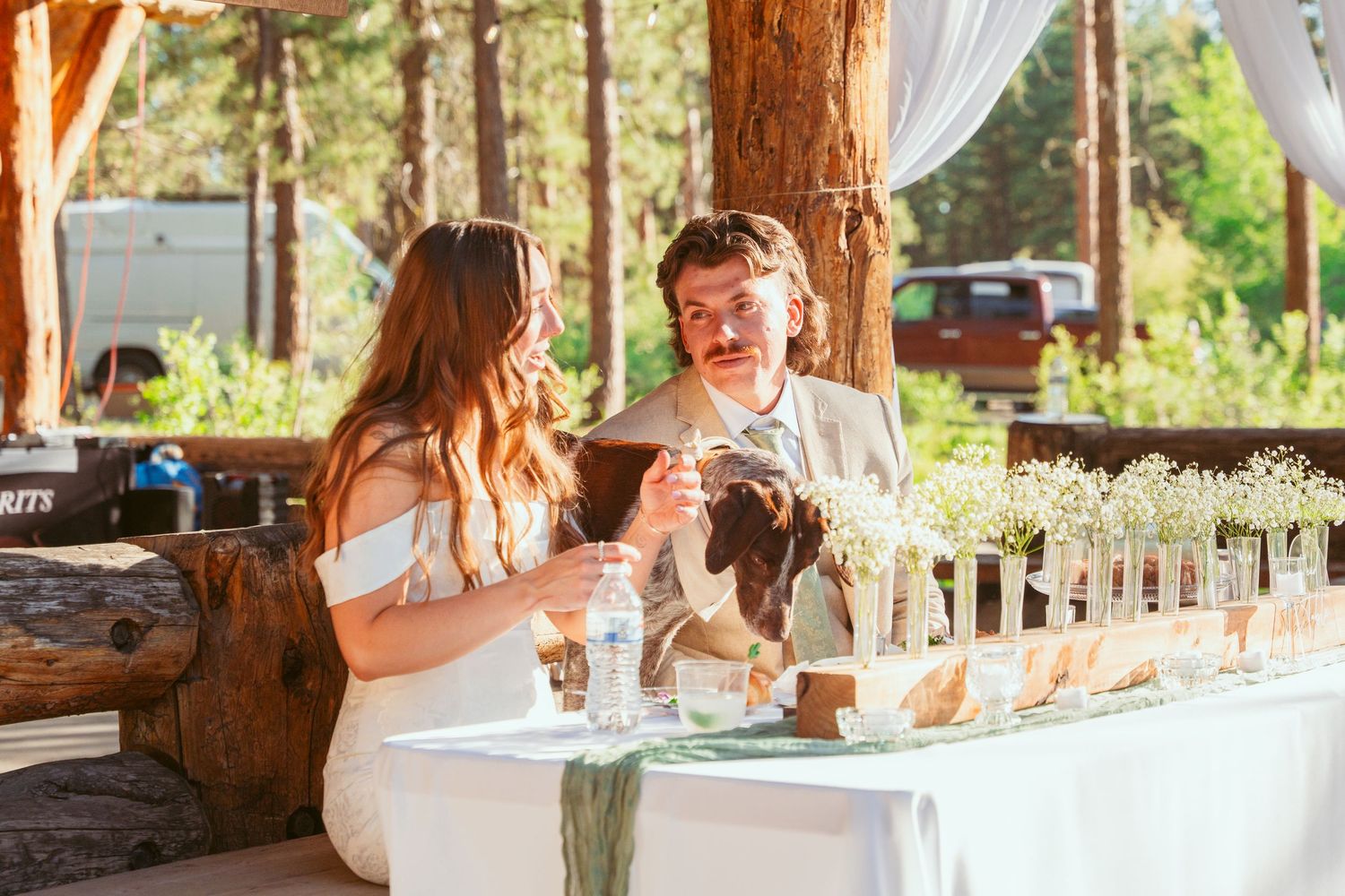 Couple sharing a toast at decorated reception table in outdoor forest venue.