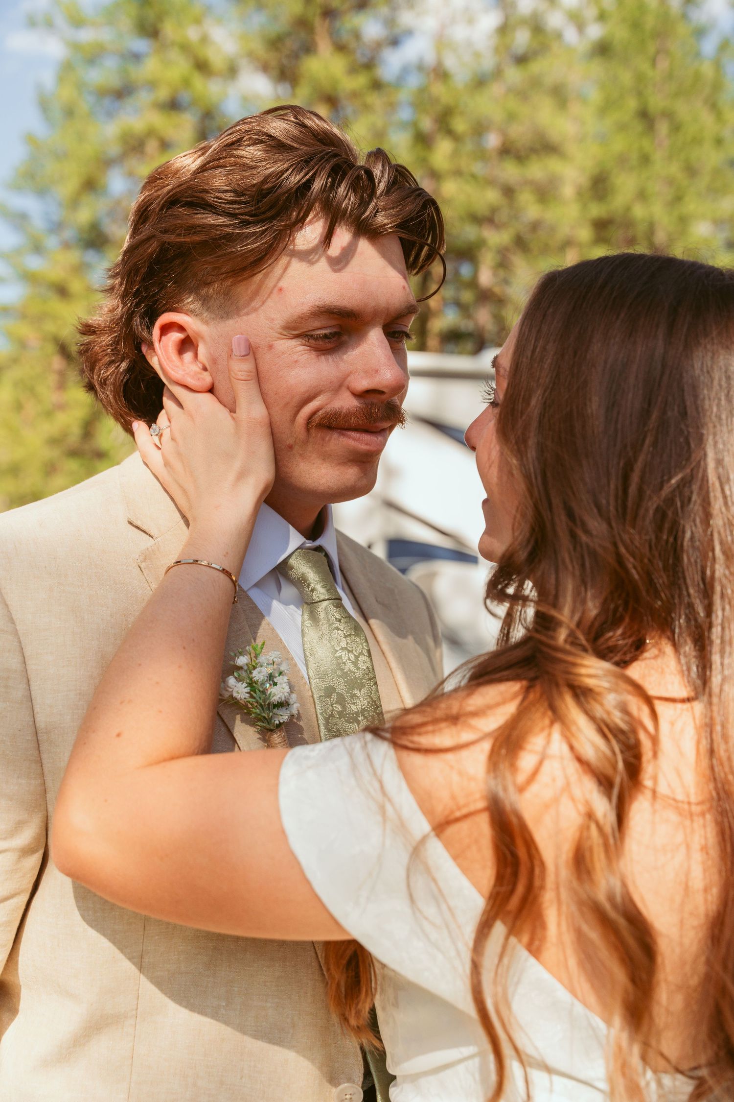 Romantic couple sharing intimate moments in a sunlit outdoor setting with pine trees in the background.