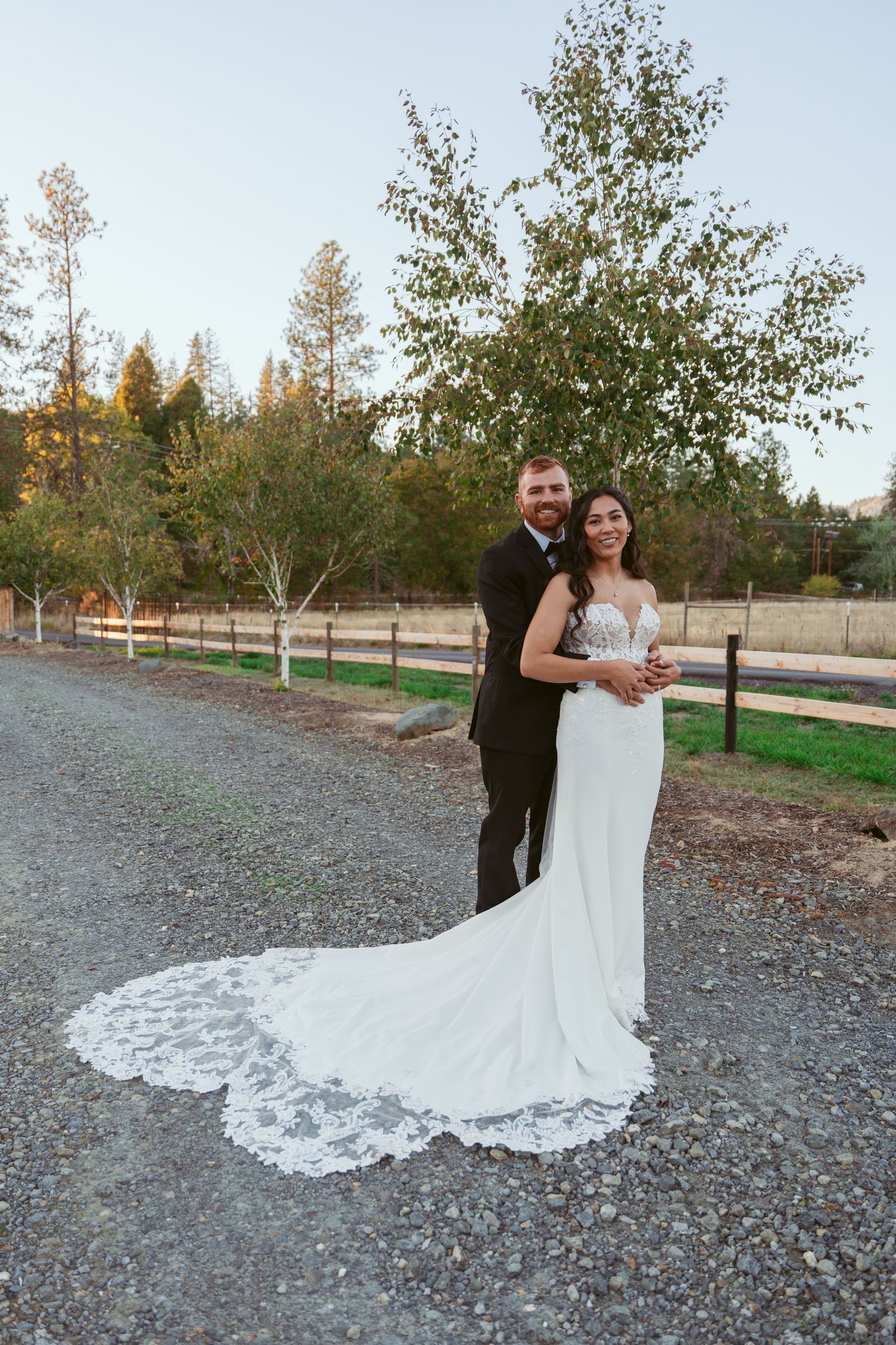 Elegant bride in lace wedding dress with dramatic train poses outdoors.