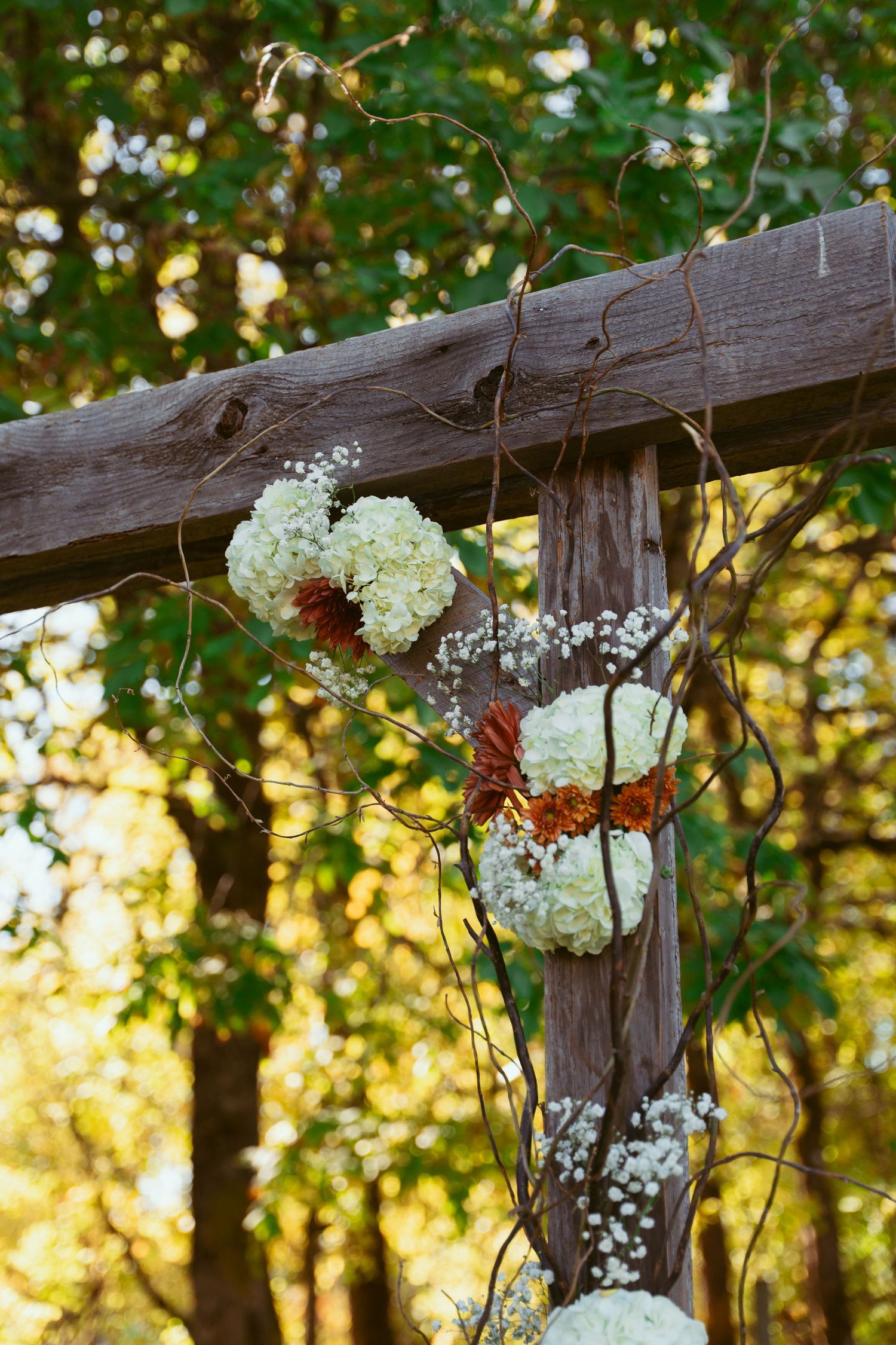 White hydrangeas and floral decorations adorning wooden cross at outdoor ceremony.