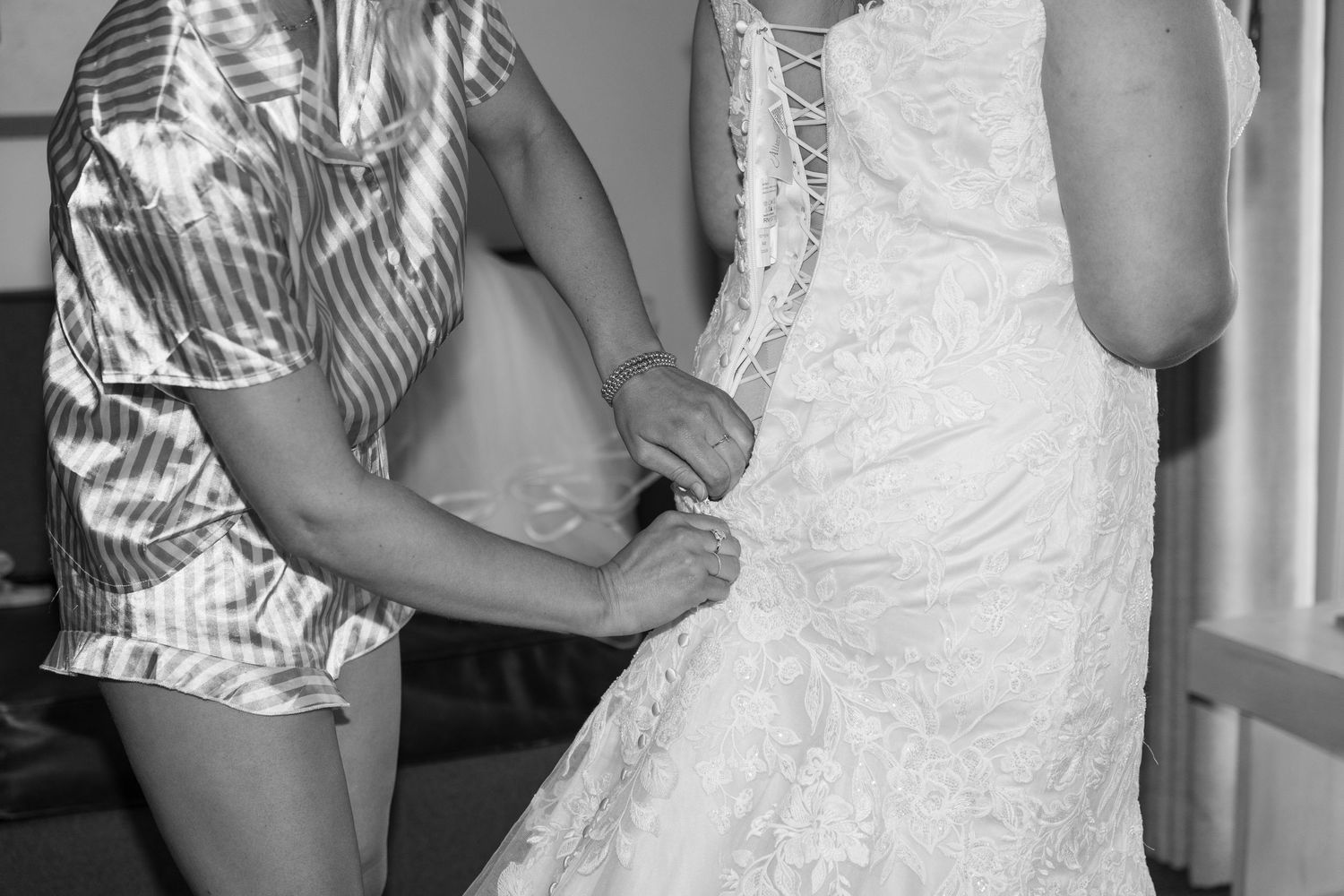 Close-up black and white detail of hands adjusting the back of a lace wedding dress.