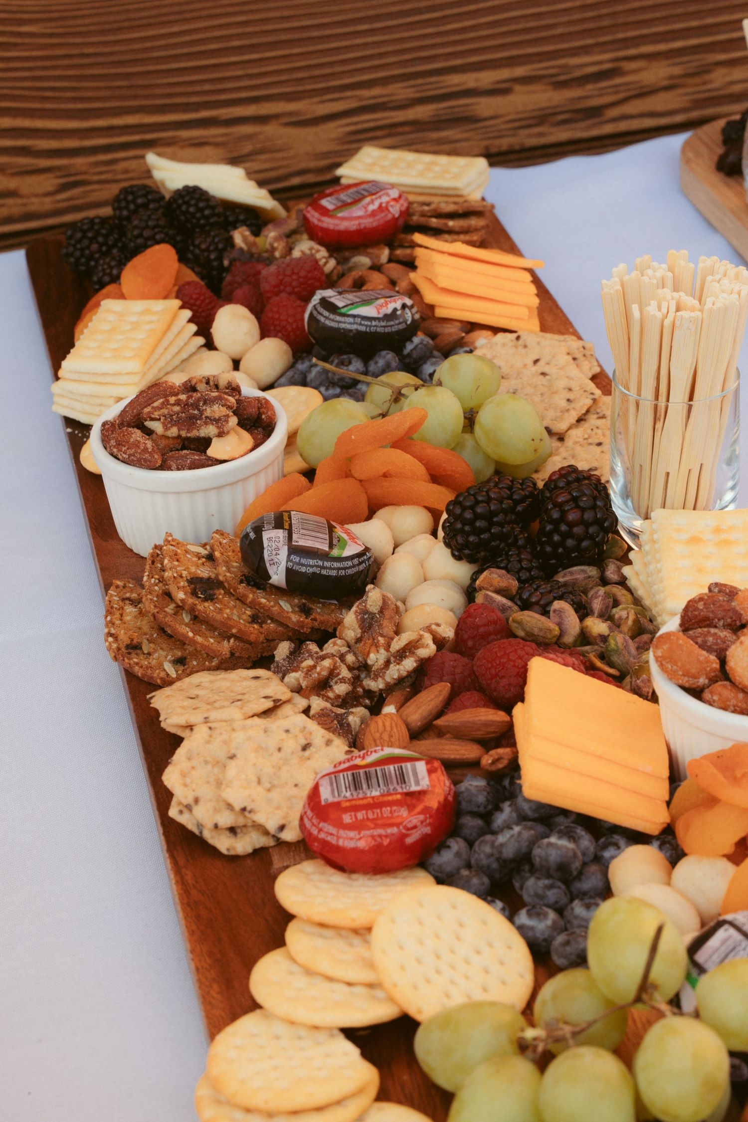 Gourmet cheese board with fresh fruit, crackers, and assorted meats on wooden serving platter.