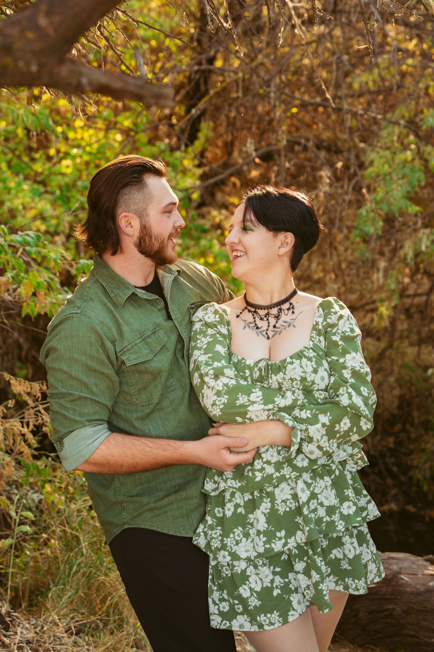 A romantic couple shares laughter while sitting together in a natural outdoor setting.