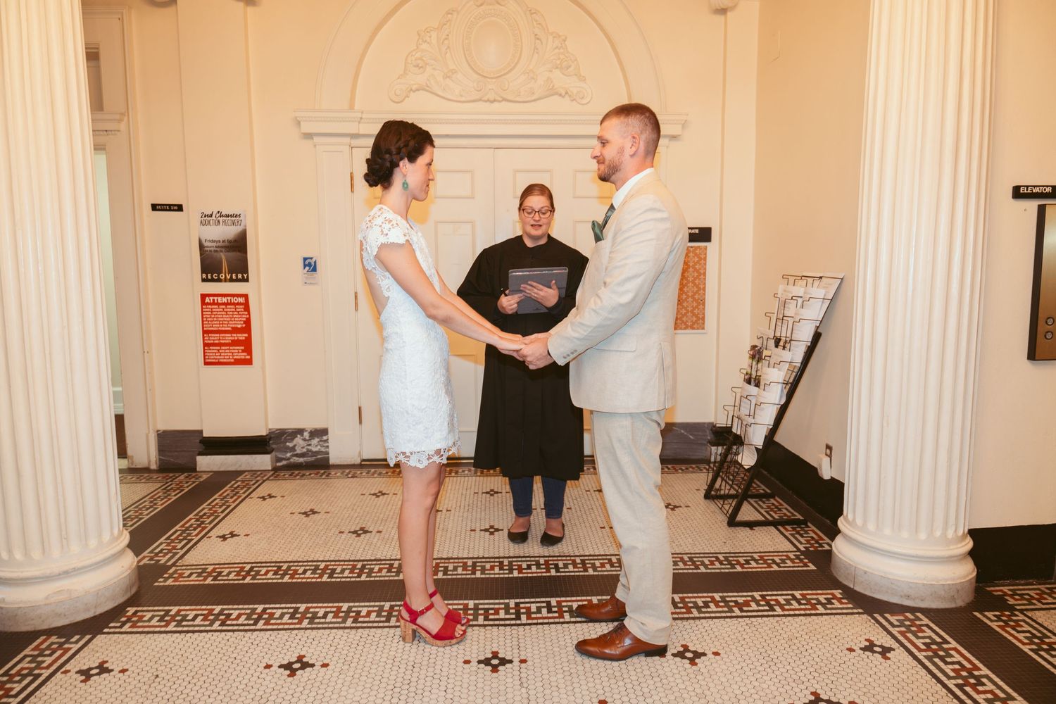 A wedding ceremony taking place in an elegant room with white columns and decorative molding.