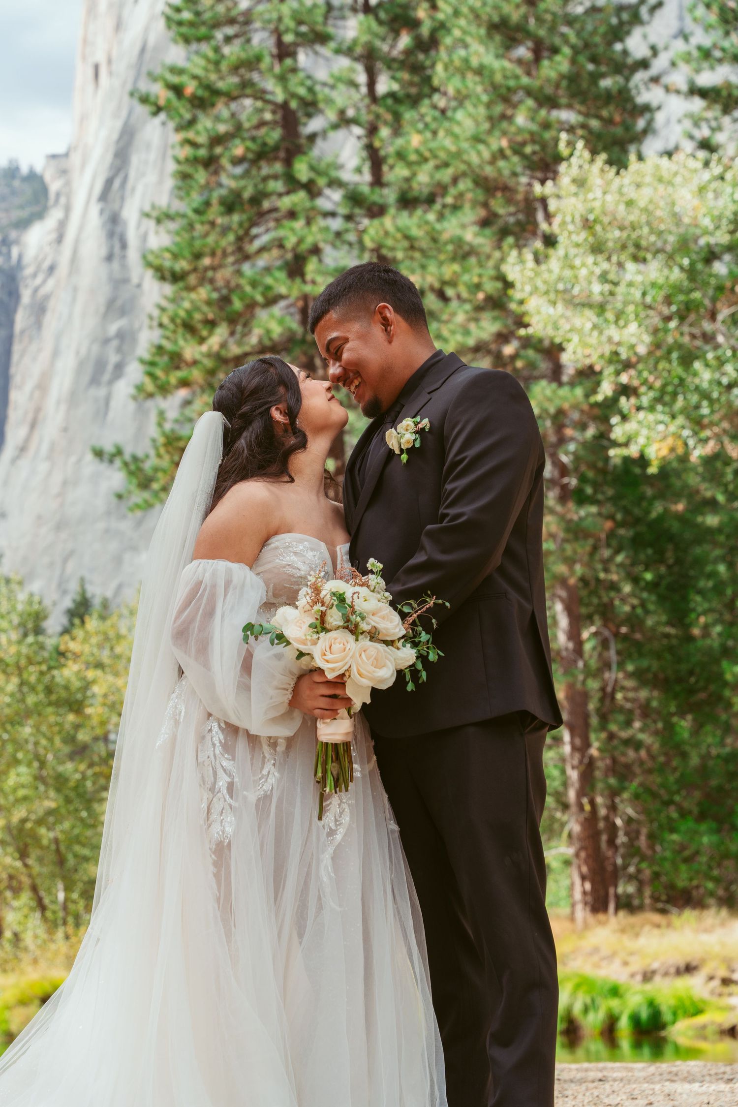 Wedding couple embracing in front of majestic Yosemite cliffs and pine trees.