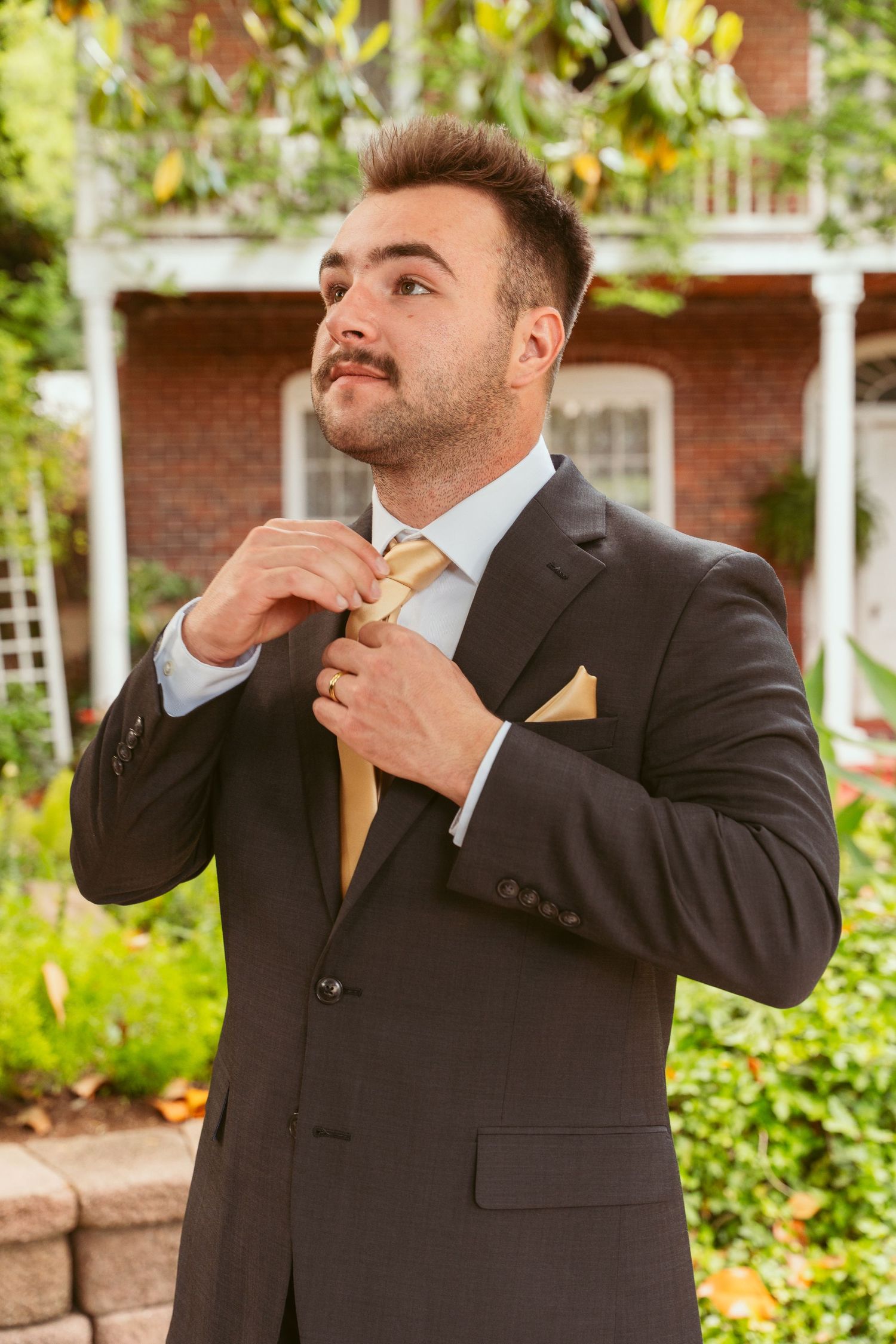 Groom in formal attire with yellow tie making playful poses during wedding photoshoot.