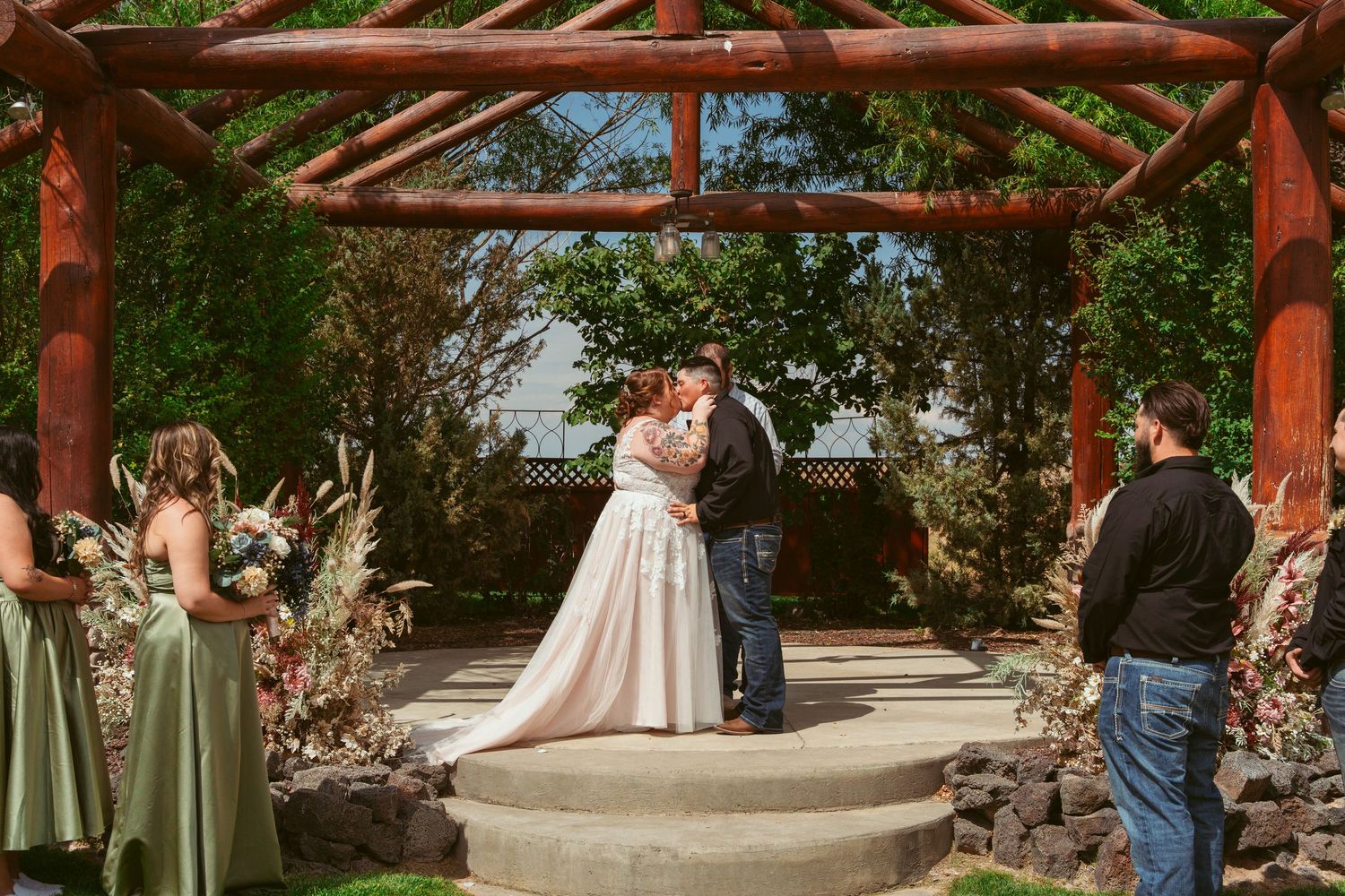 A panoramic view of a wedding ceremony setup with wooden pergola and white chairs on a grassy lawn.