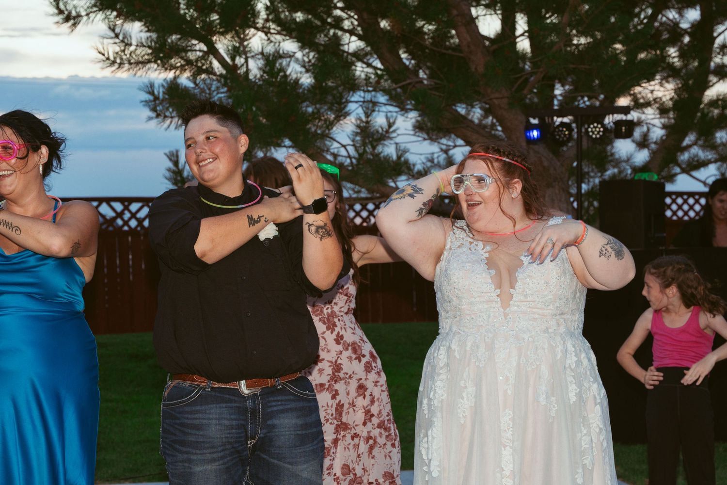 Group of wedding guests performing synchronized dance moves at an outdoor reception.