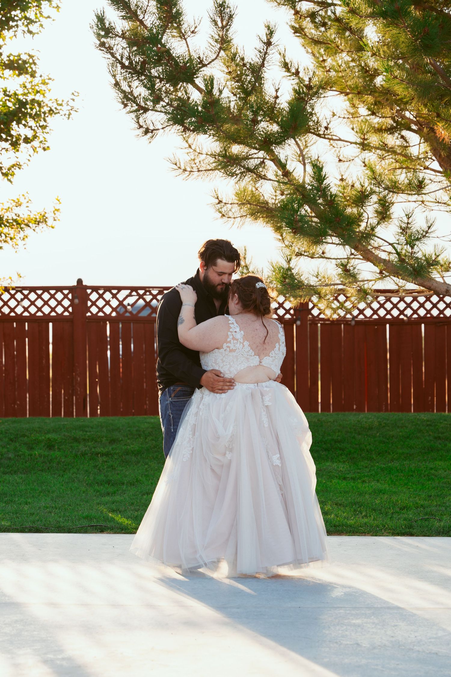 A couple shares their first dance on an outdoor dance floor with a wooden fence backdrop.