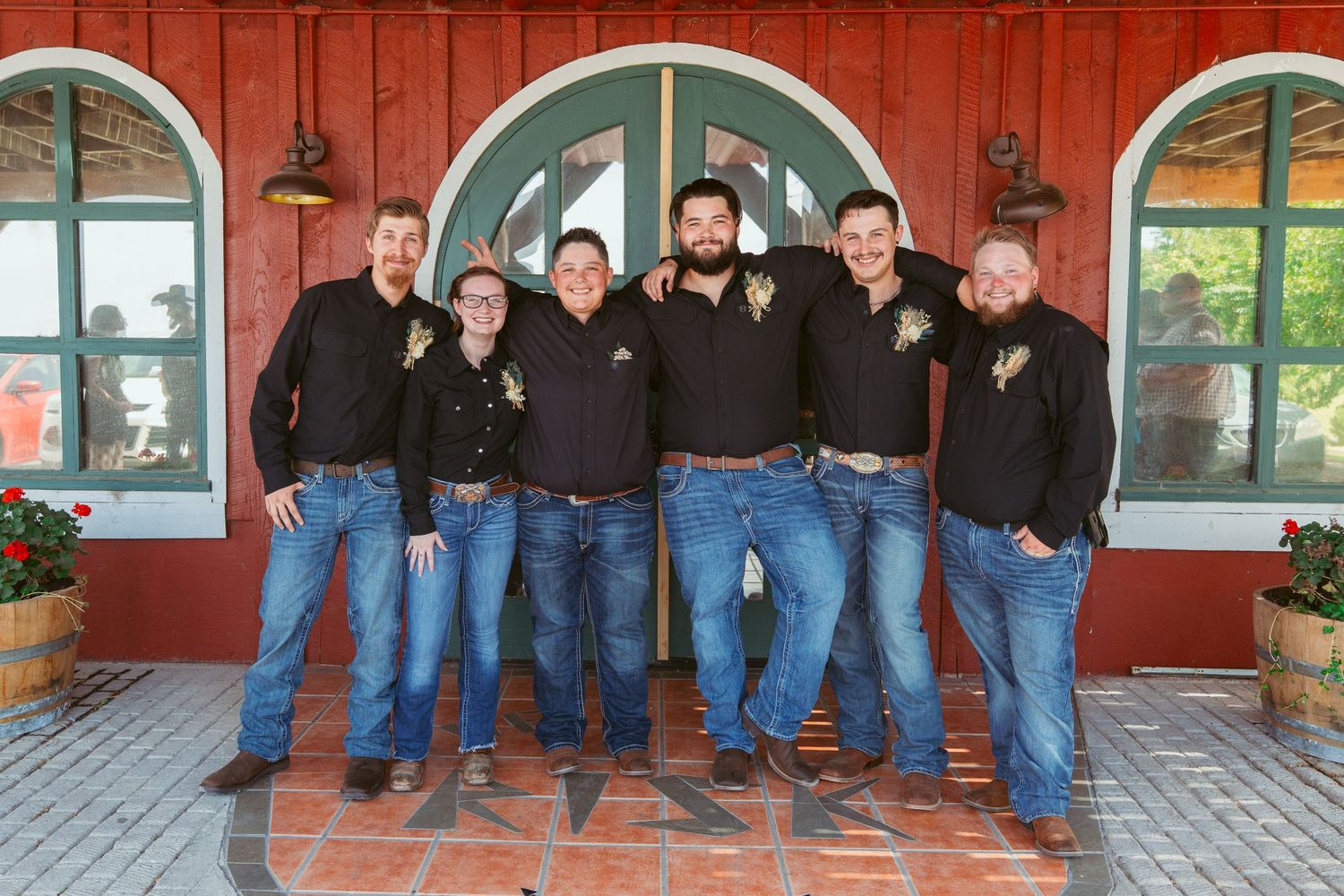 Group wearing matching jeans and black tops sitting along red building porch.