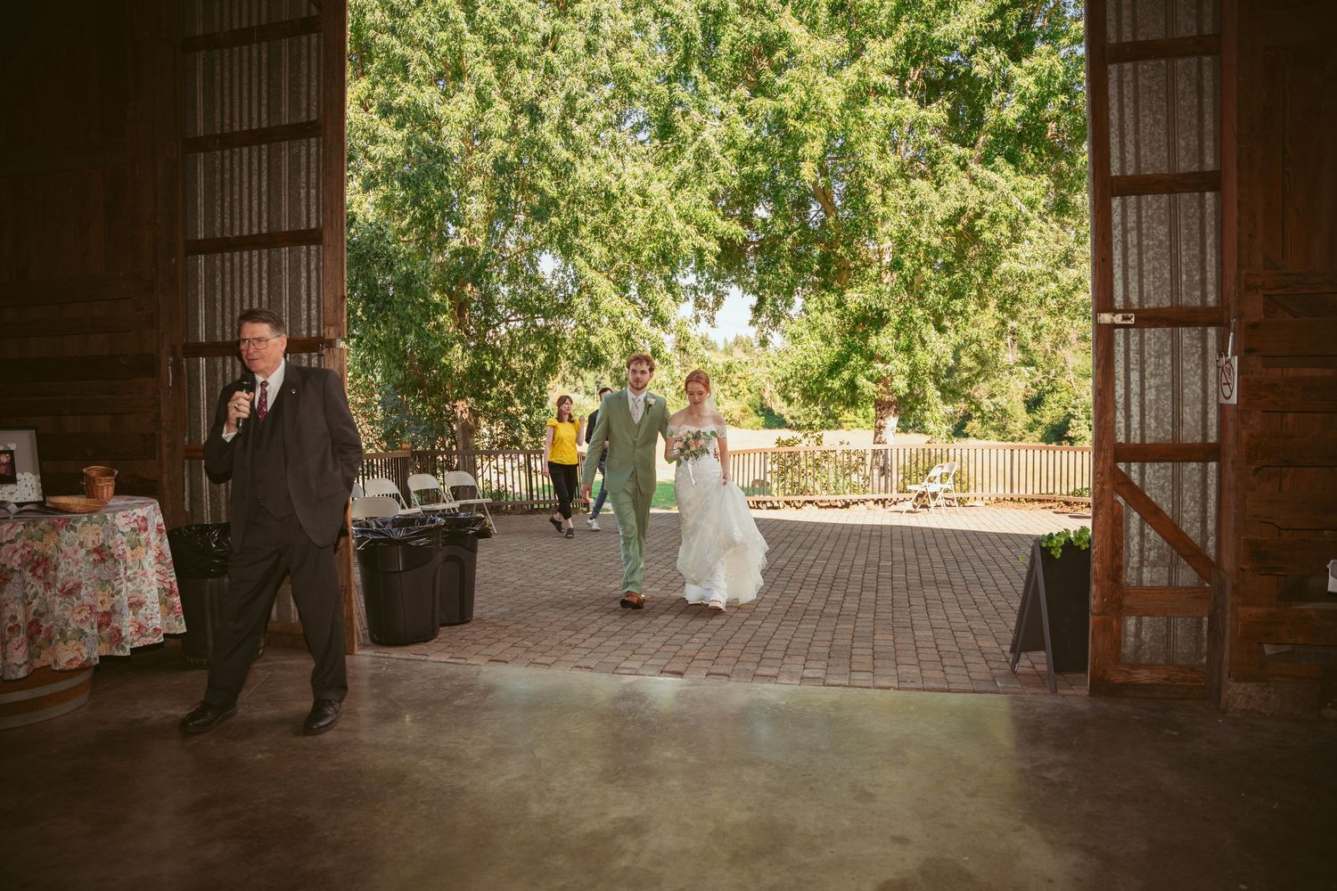 Rustic barn wedding venue interior with brick floor and large open doors leading to garden.
