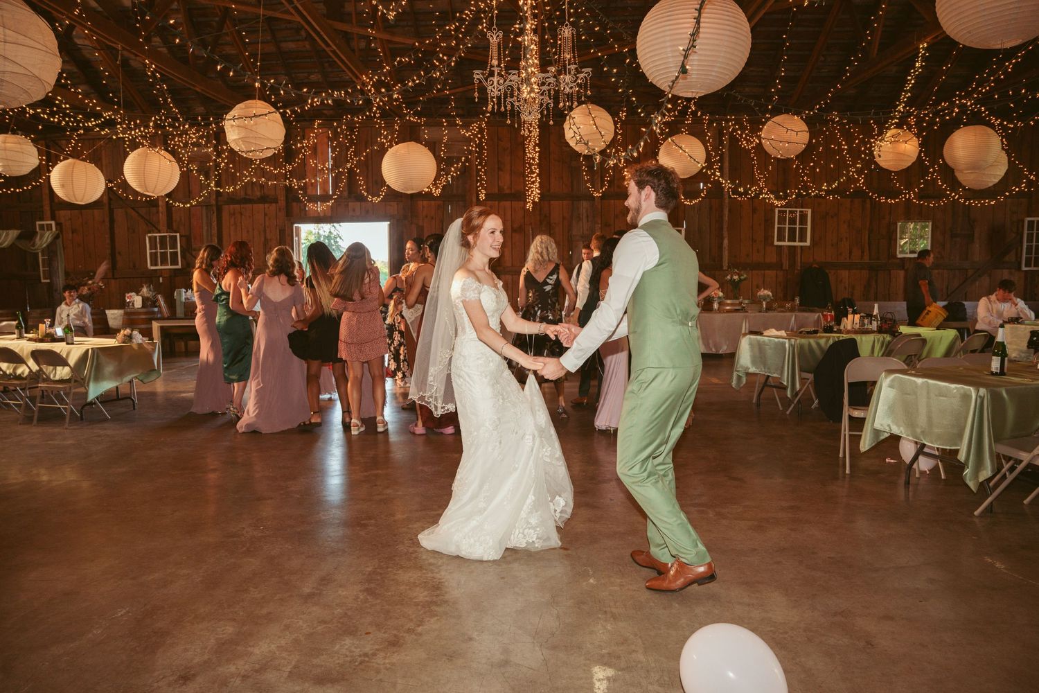 Newlyweds dancing in a rustic barn venue decorated with string lights and paper lanterns.