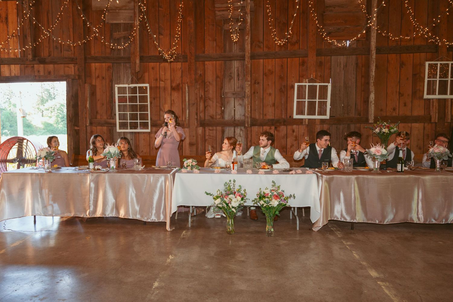 Full view of rustic barn wedding reception with guests seated at decorated tables.