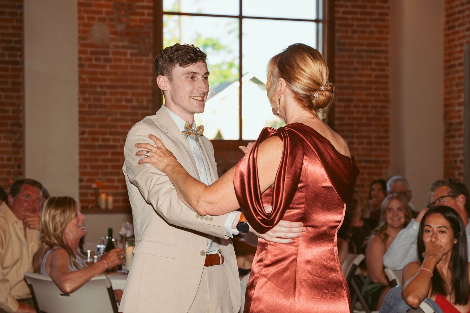 Couples swing dancing at a wedding reception in a rustic brick-walled venue.