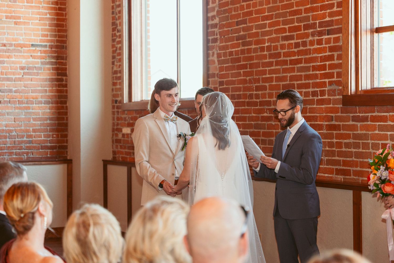 Wedding ceremony proceedings in an elegant brick-walled venue with bright windows.