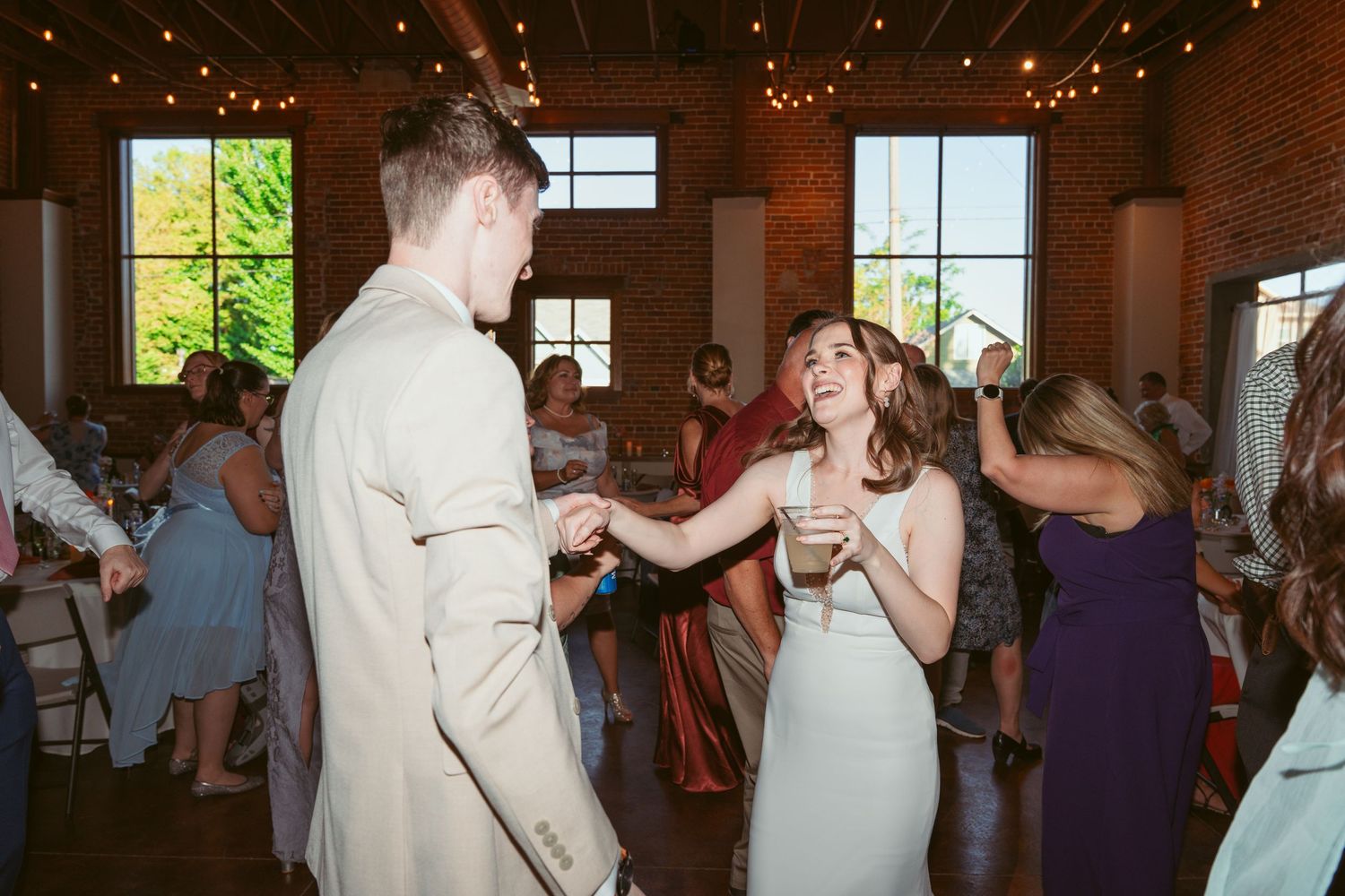 Guests enjoying themselves on the dance floor at an indoor wedding reception with exposed brick walls.