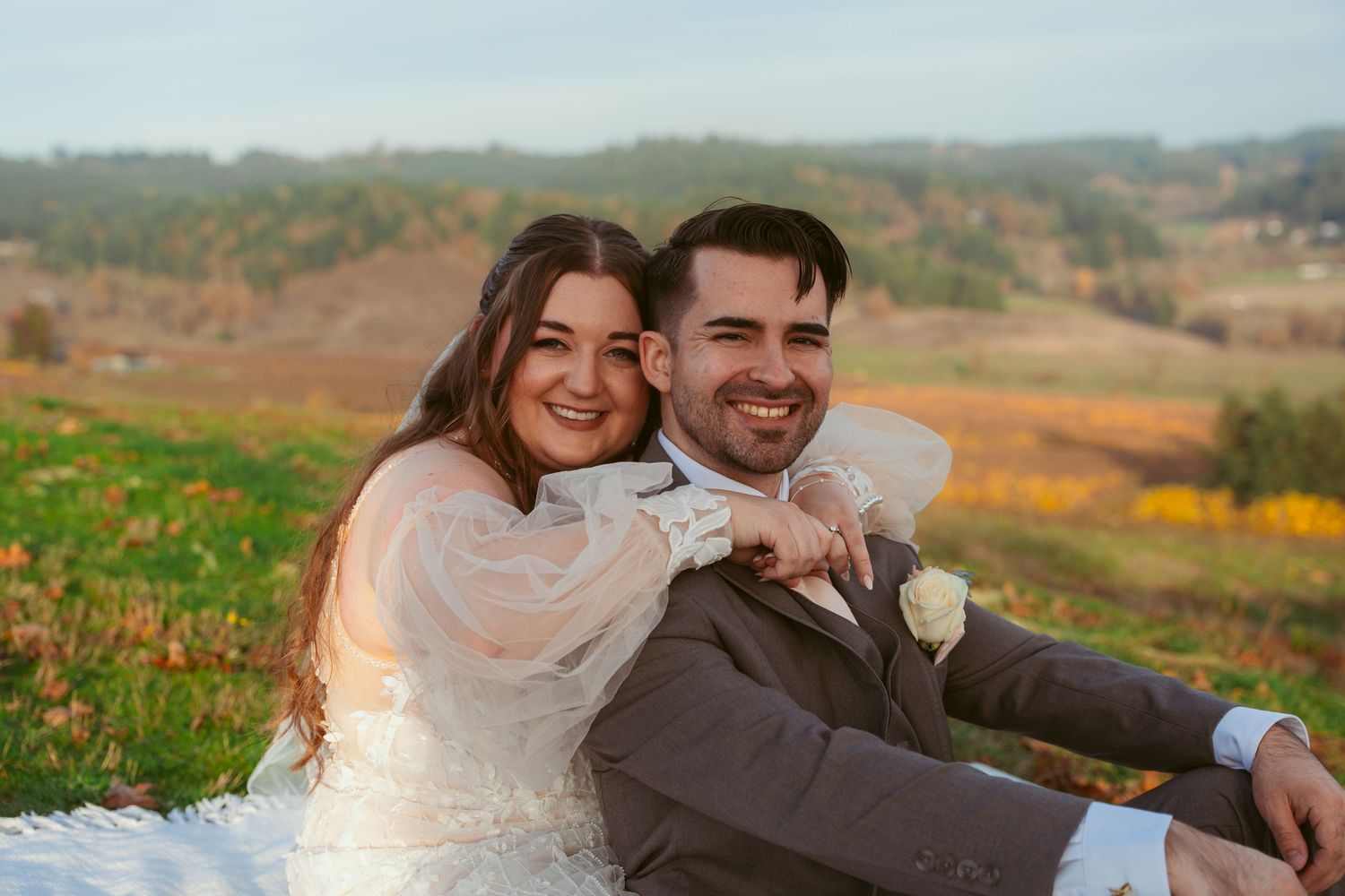 Wedding couple laughing together on a hillside with fall colors in the background.