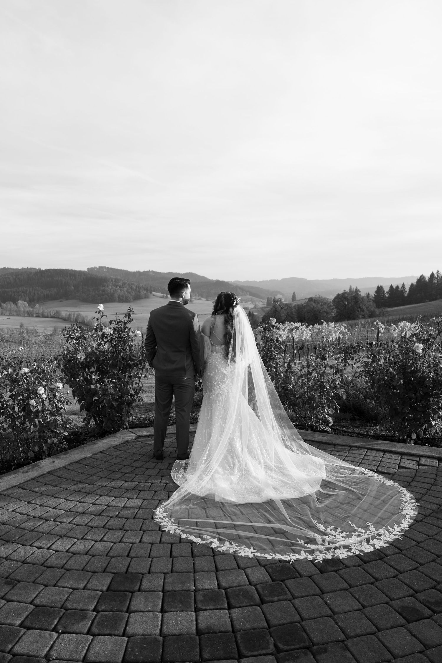 Black and white wedding portrait showing dramatic veil spread across brick patio.