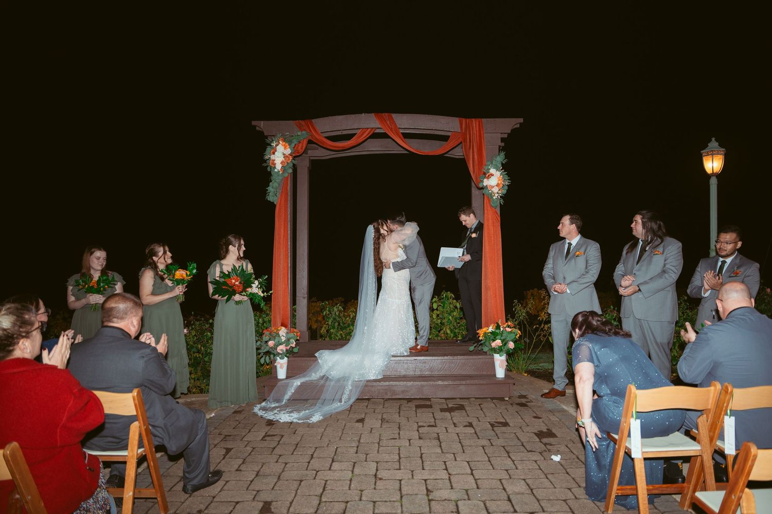 Wedding ceremony at night with guests seated on a paved courtyard under string lights.