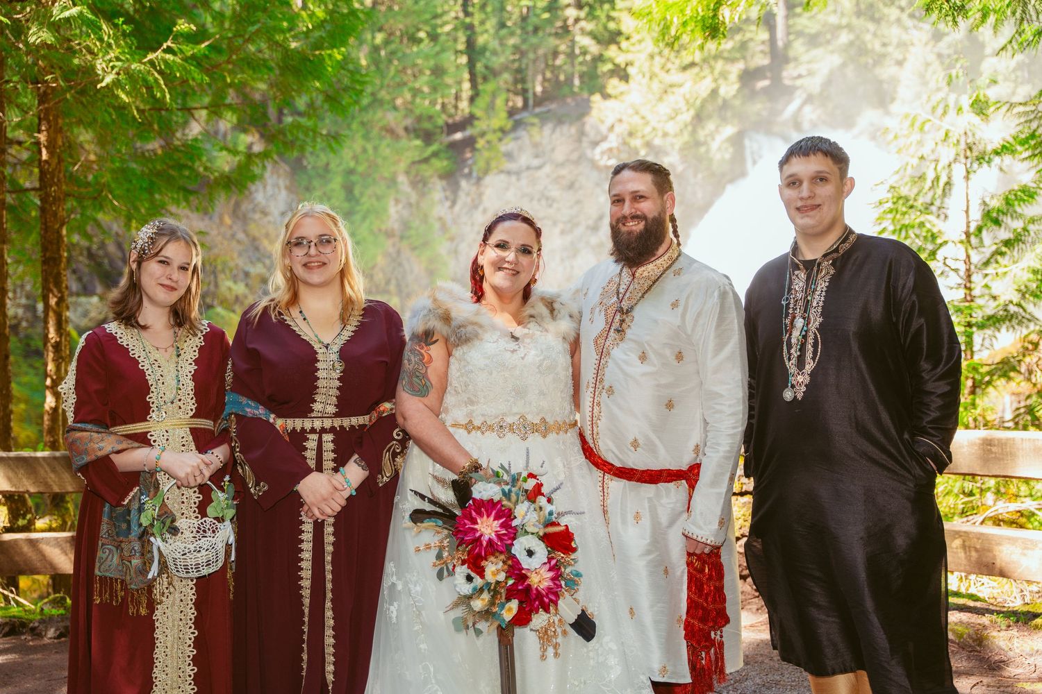 Wedding party arranged for photos with burgundy and white color scheme in woodland setting.