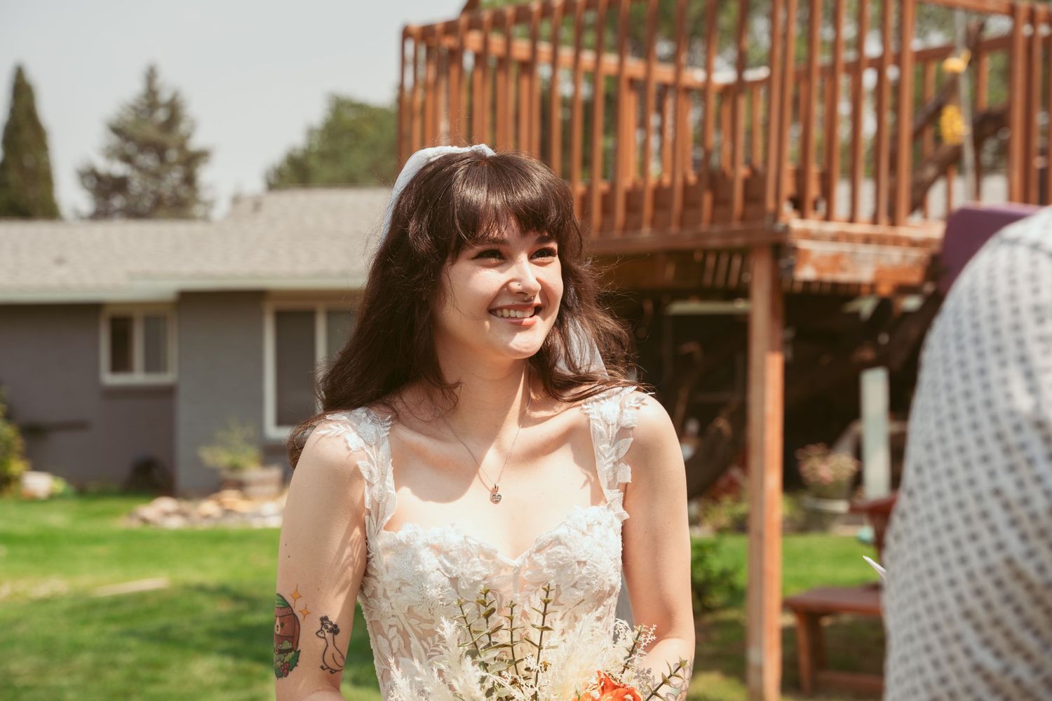 A bride in a lace wedding dress smiles brightly in a backyard setting.