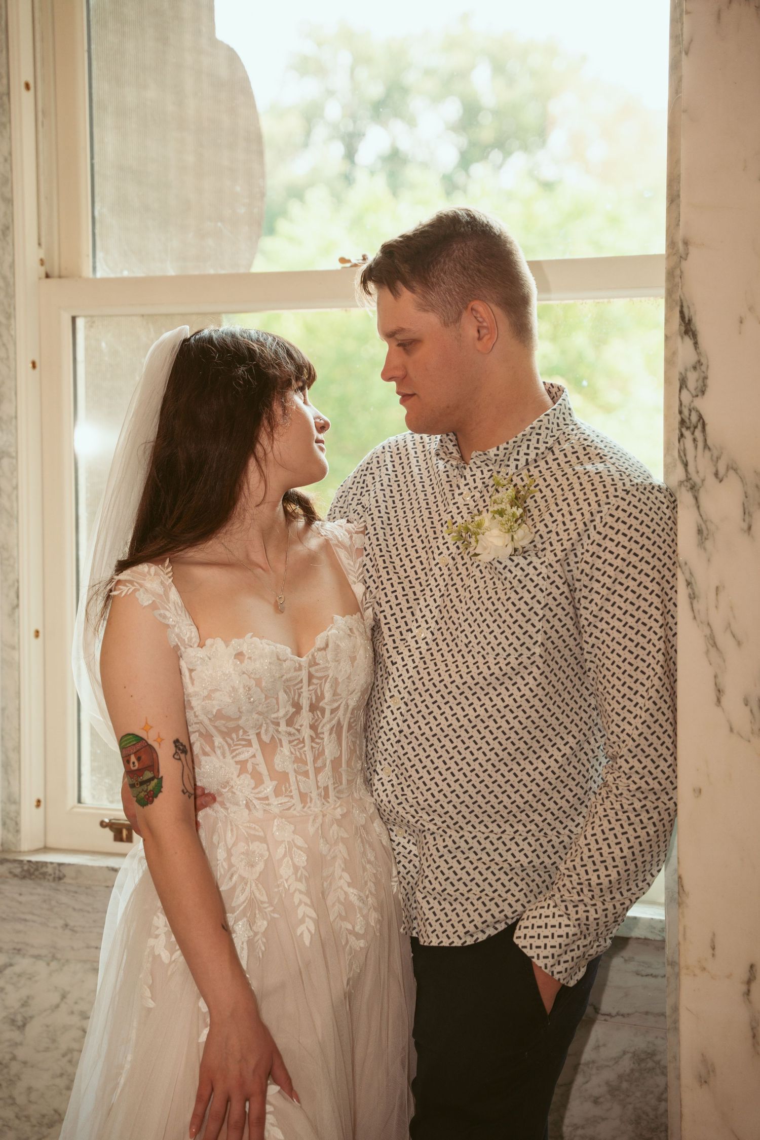 A couple shares tender moments in a sunlit room with white walls and windows.