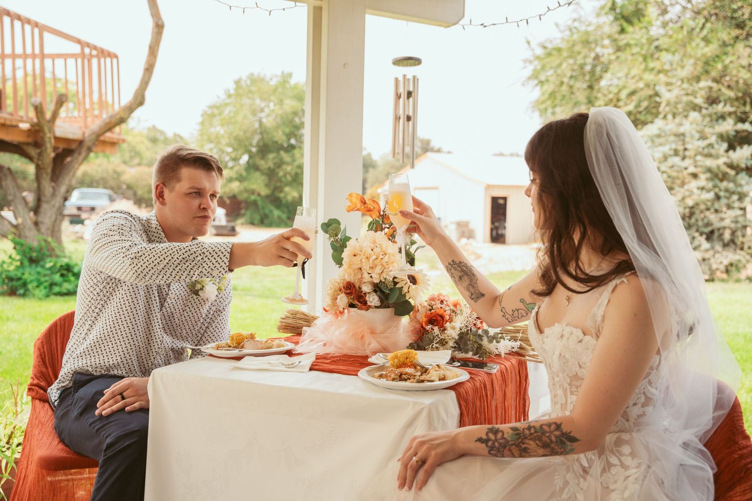 Wedding reception table settings with orange and white decor in a sunlit venue.