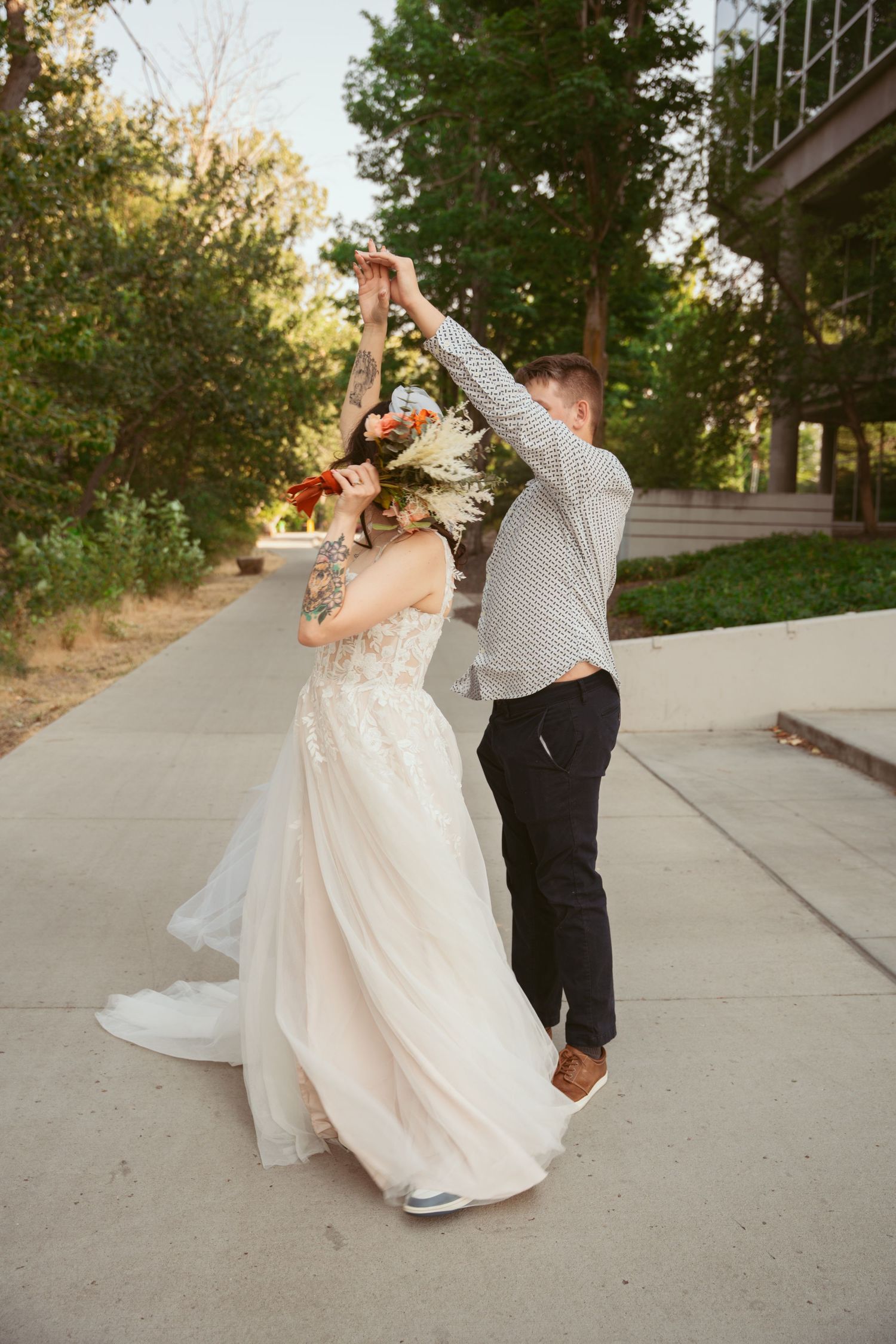 Wedding couple dancing and twirling on outdoor sidewalk at sunset.