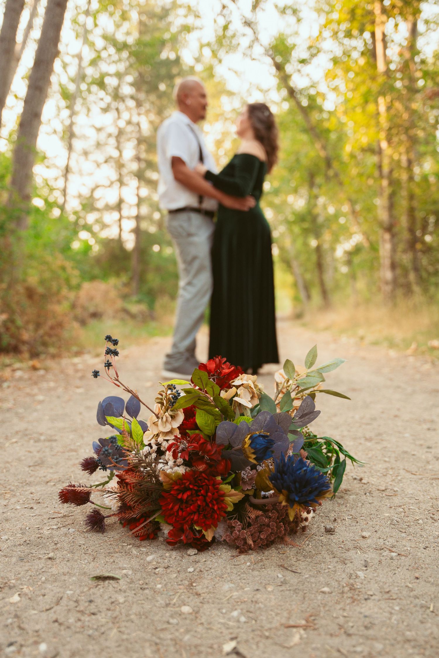 Beautiful autumn floral arrangement with red and blue flowers lies on a dirt path in a forest setting.