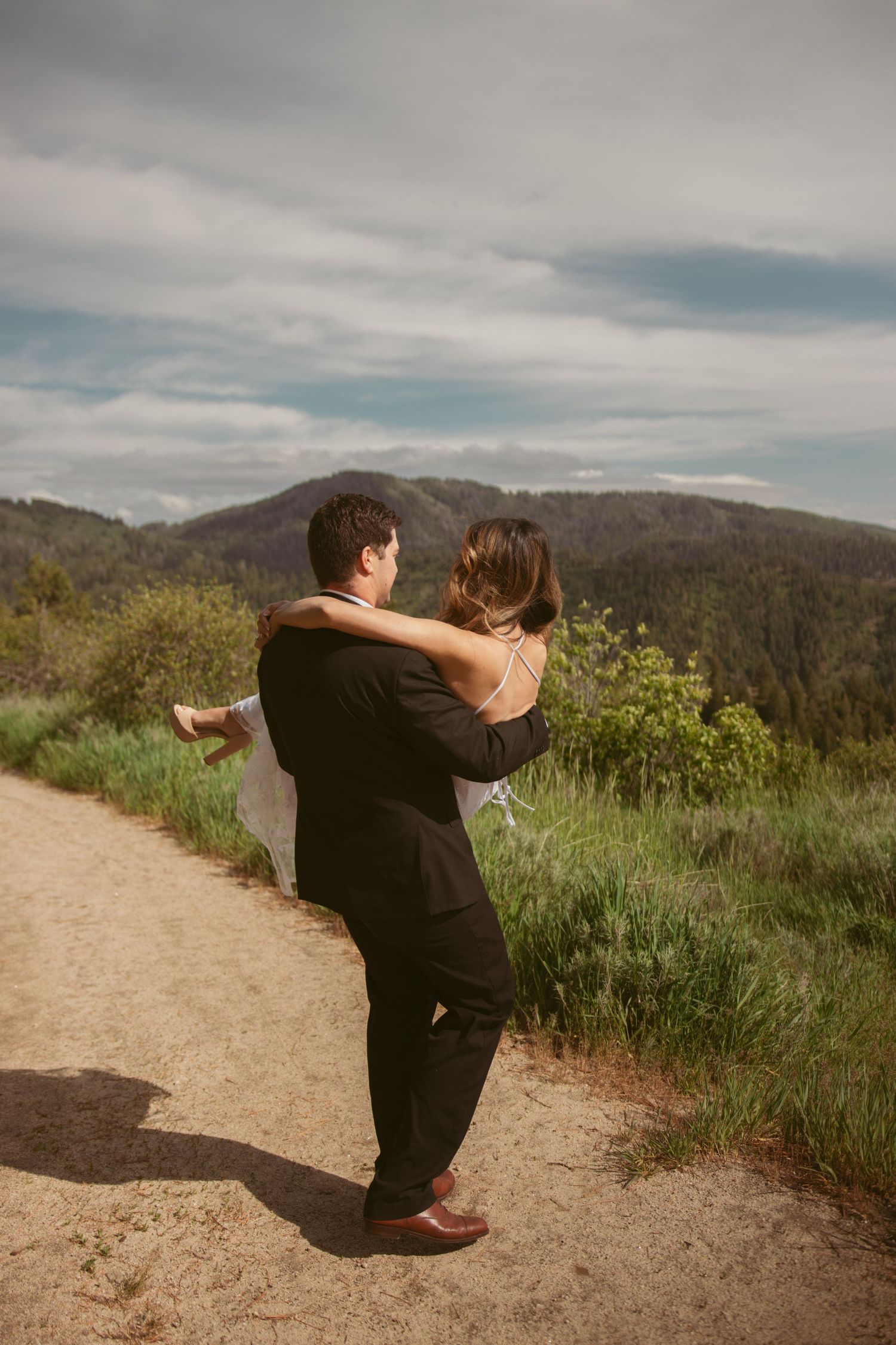 A couple performs a dramatic dance lift on a scenic mountain path.