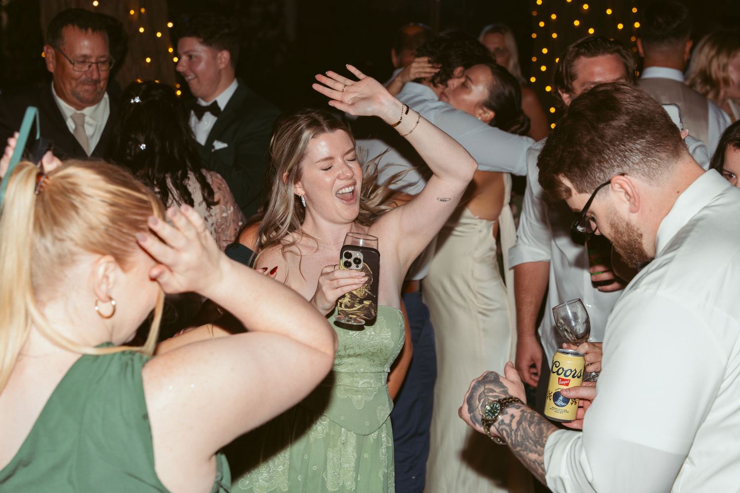 Wedding reception guests dancing and celebrating on a dance floor under string lights.
