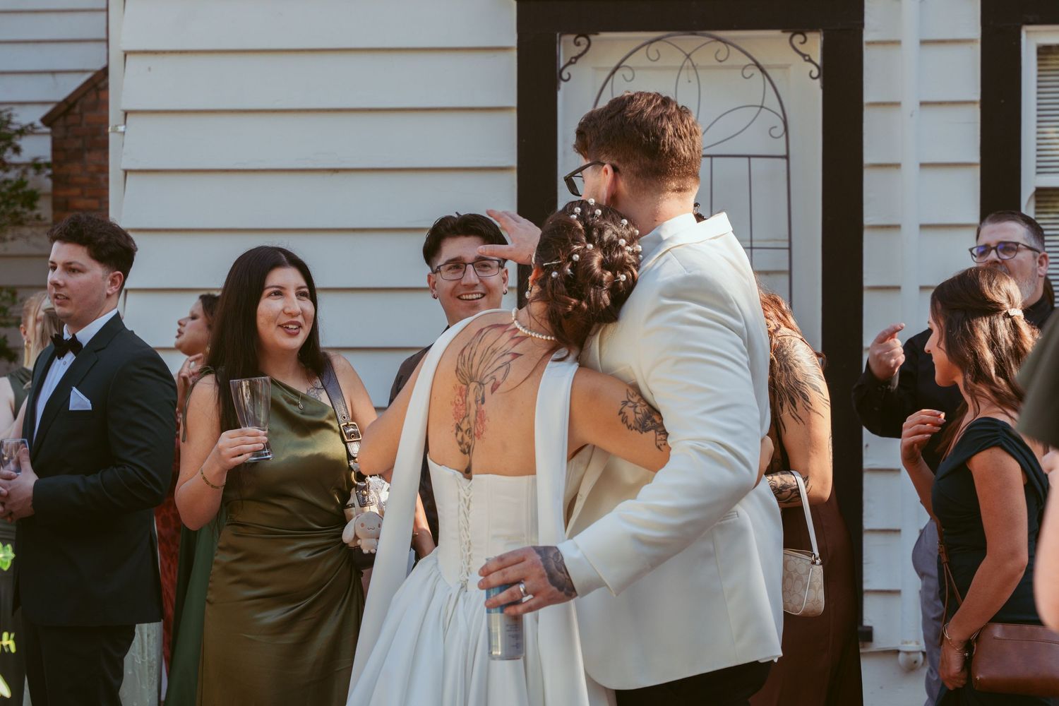 Wedding party members interacting and celebrating outside a white building during daytime.