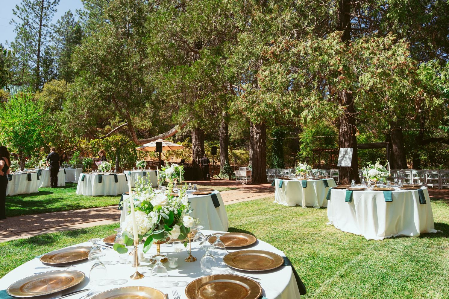 Outdoor wedding reception setup with white chairs and floral arrangements in a garden setting.