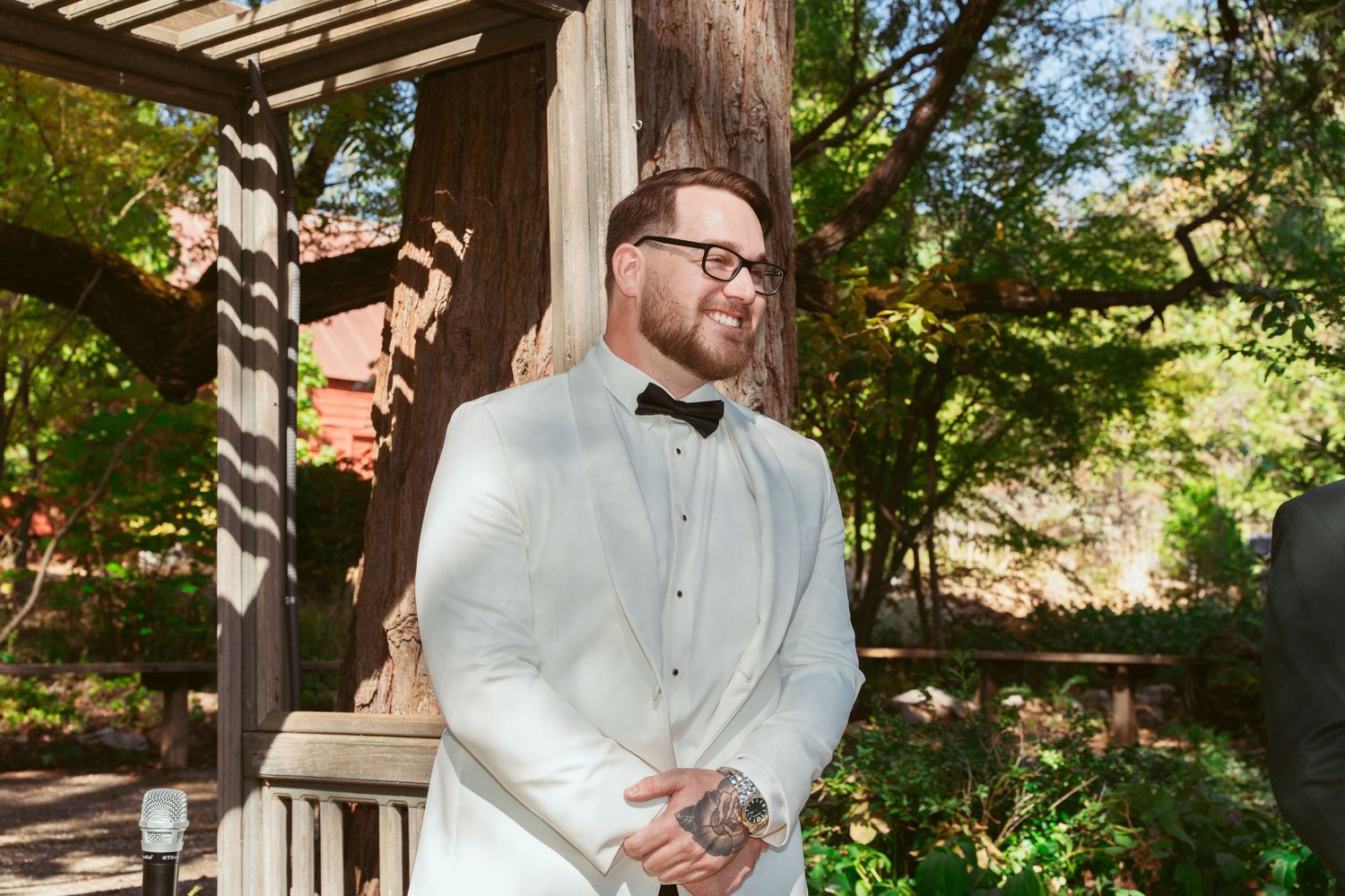 Couple exchanges vows under rustic wooden pergola in garden setting.