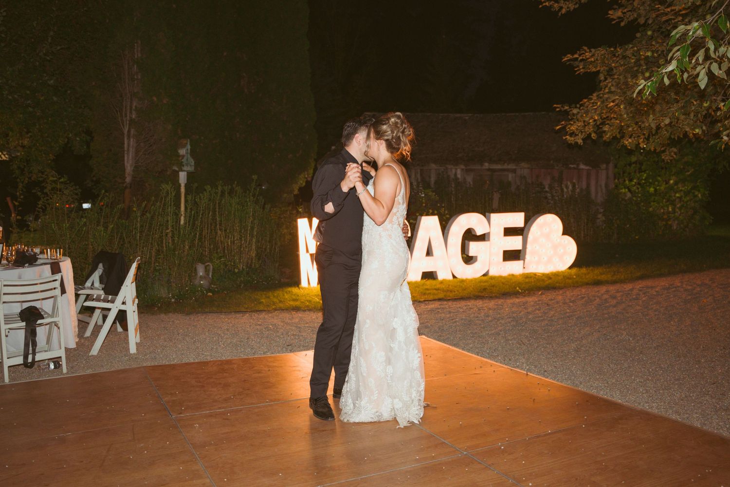 A couple shares a romantic dance moment with illuminated SAGE sign glowing behind them.
