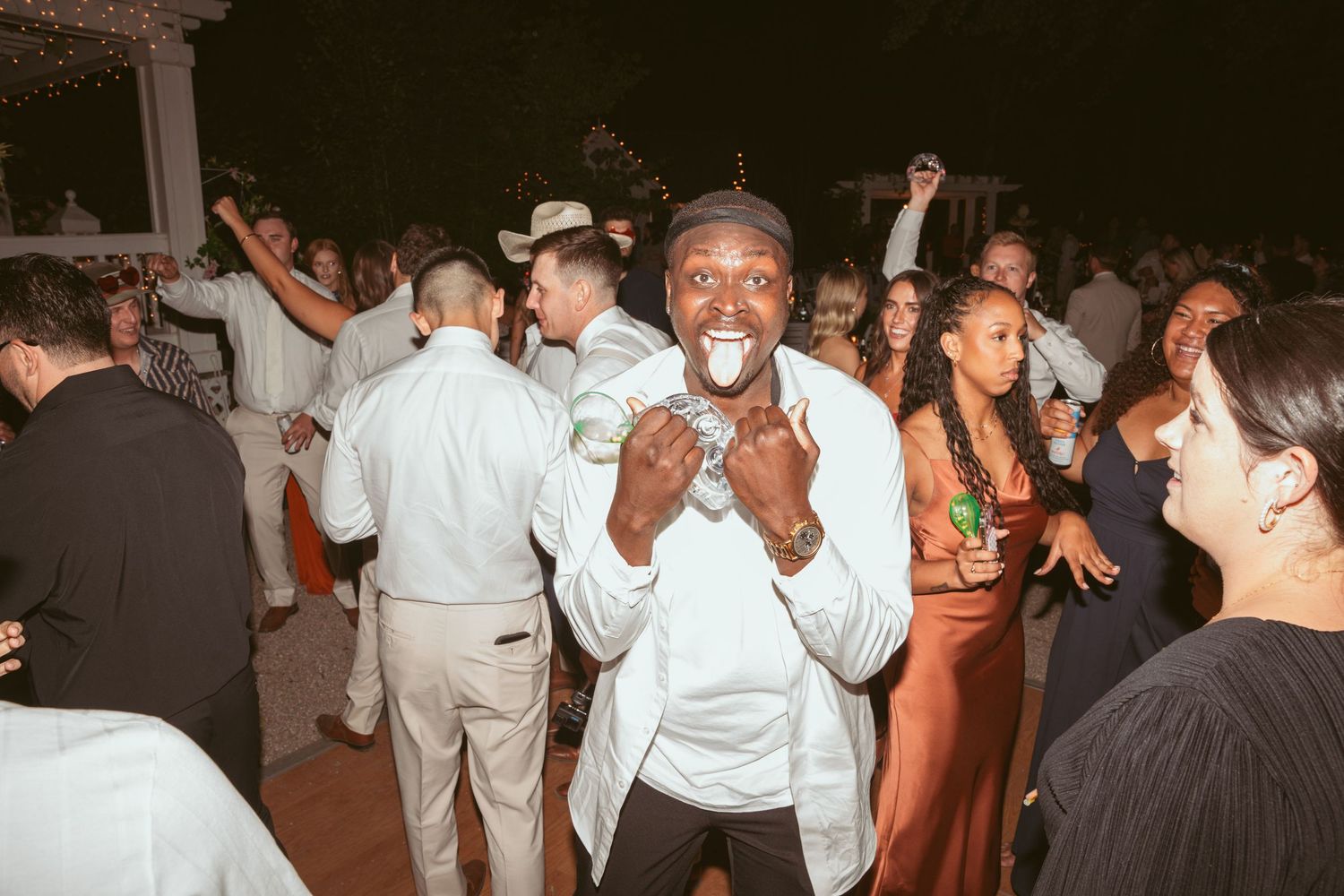 Large group of wedding guests dancing together at an outdoor evening celebration.