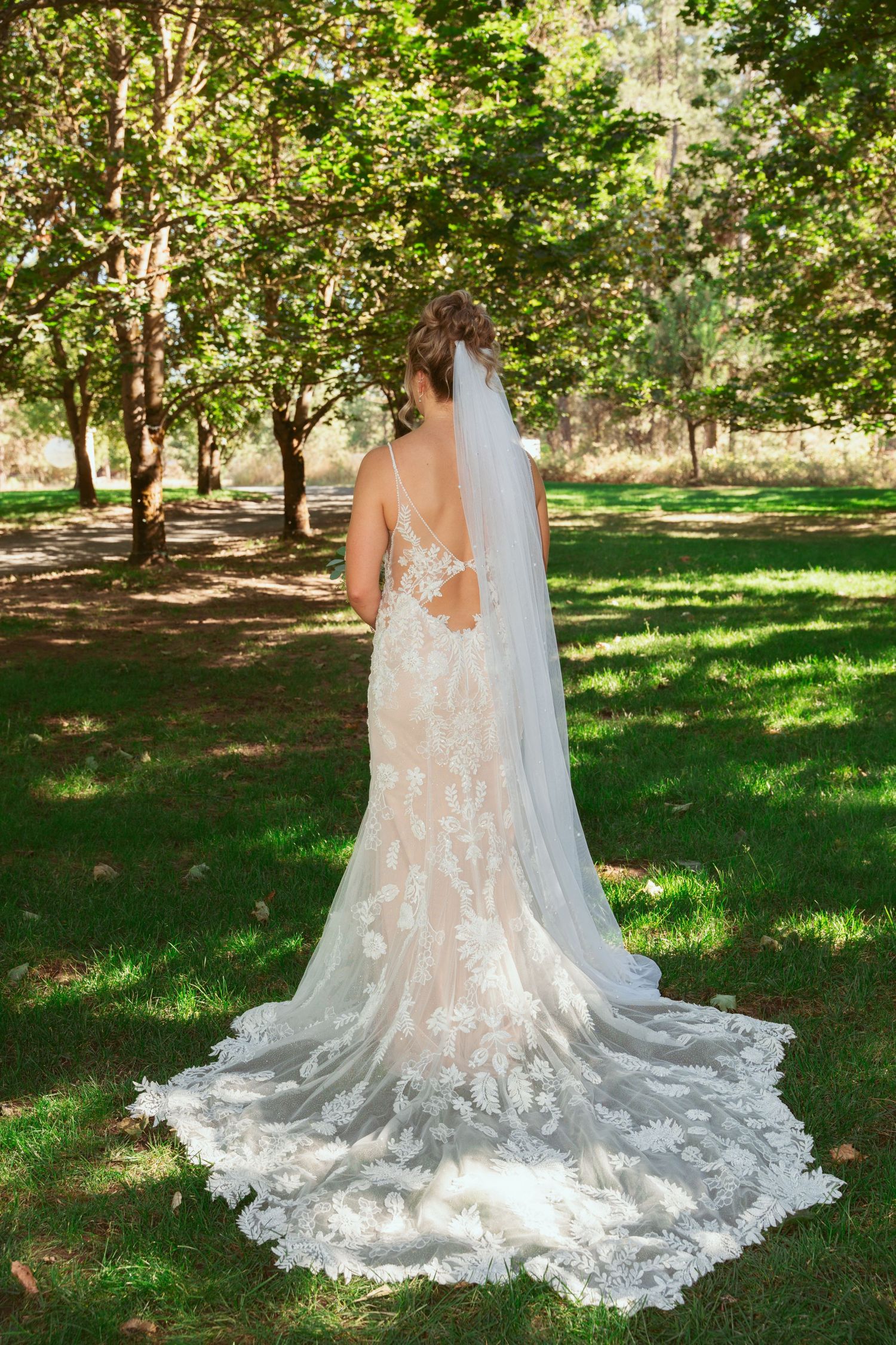 A detailed view of an elegant lace wedding dress train spread out on green grass.