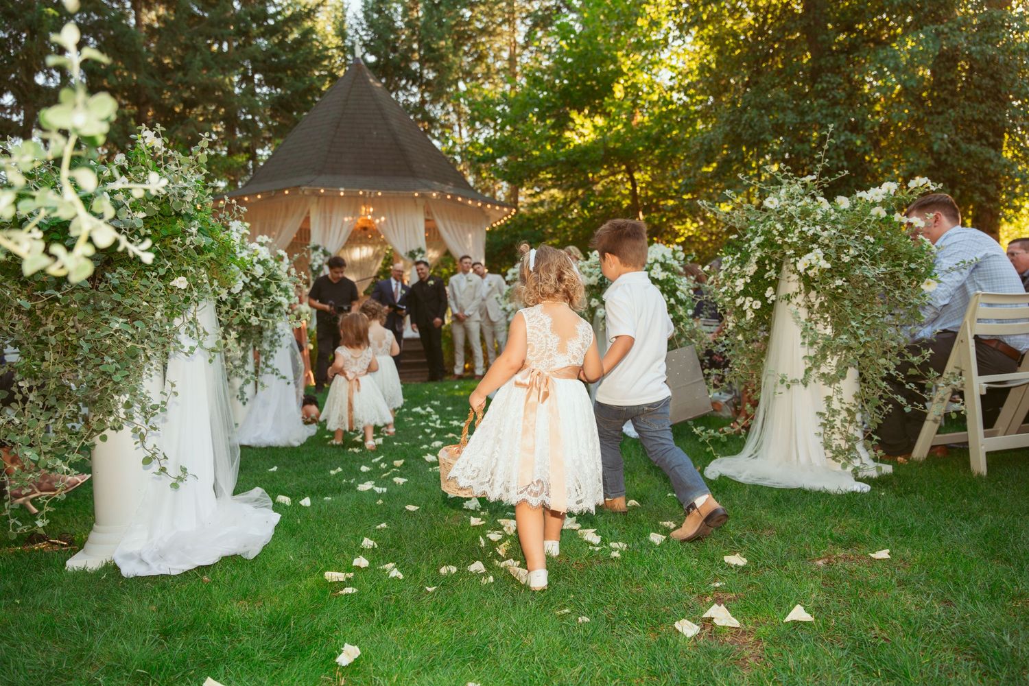 Wedding celebration in progress at outdoor garden venue with white gazebo and seated guests.