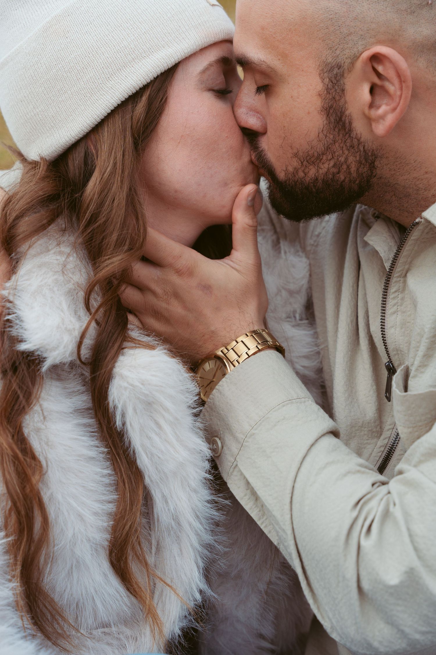A romantic couple shares an intimate moment wearing neutral tones against a blurred background.