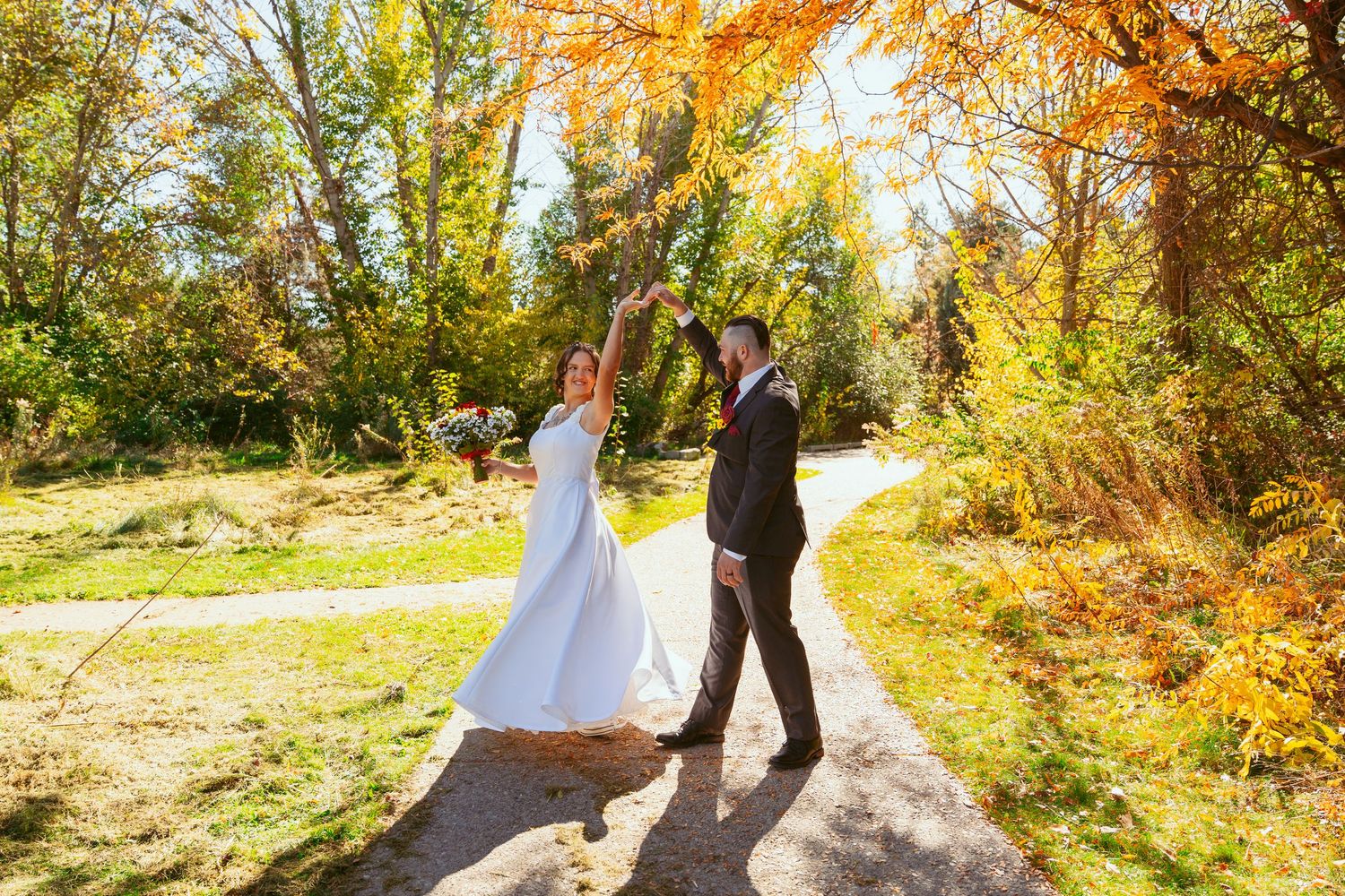 A couple shares a romantic dance on a sunlit autumn path surrounded by golden foliage.