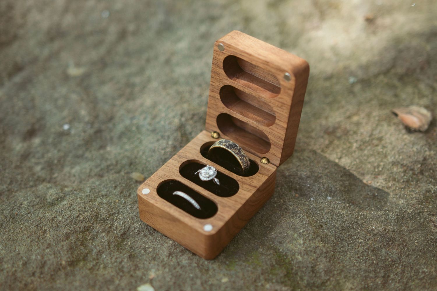Wooden ring box with hinged lid photographed on concrete surface.